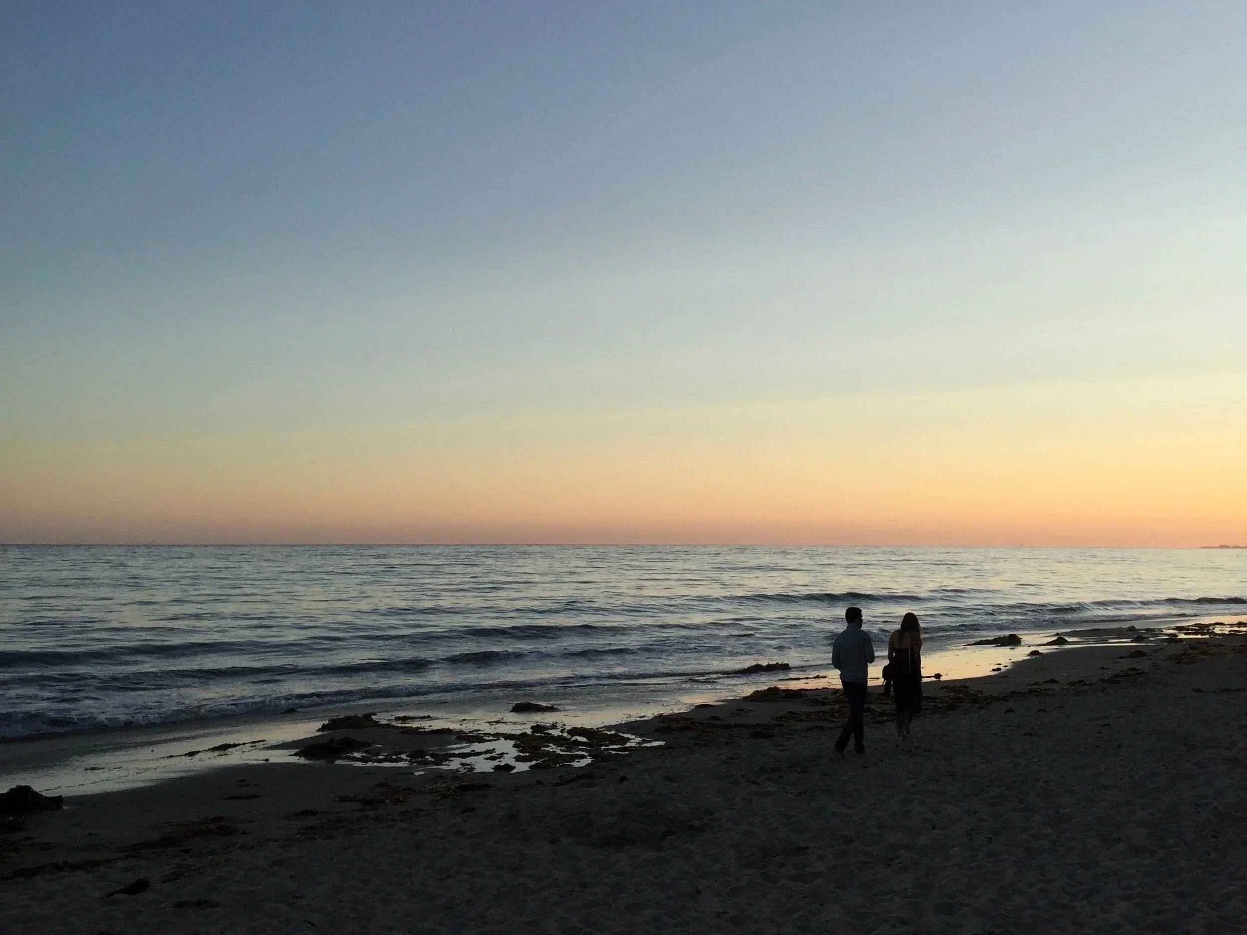 Two people walking along the beach at sunset with the ocean in the background.