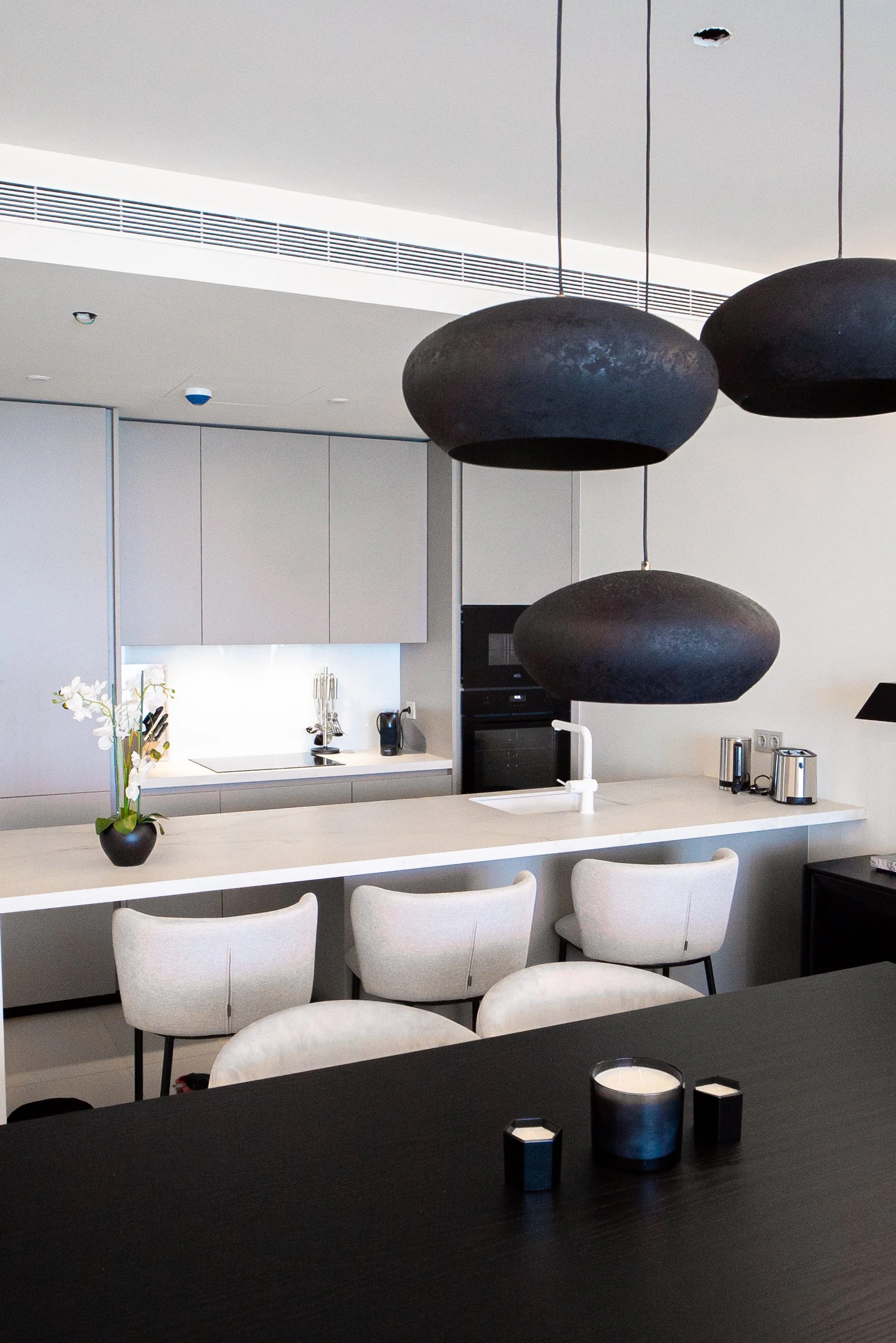 Modern kitchen with an island, white chairs, black pendant lights, and minimal decor.