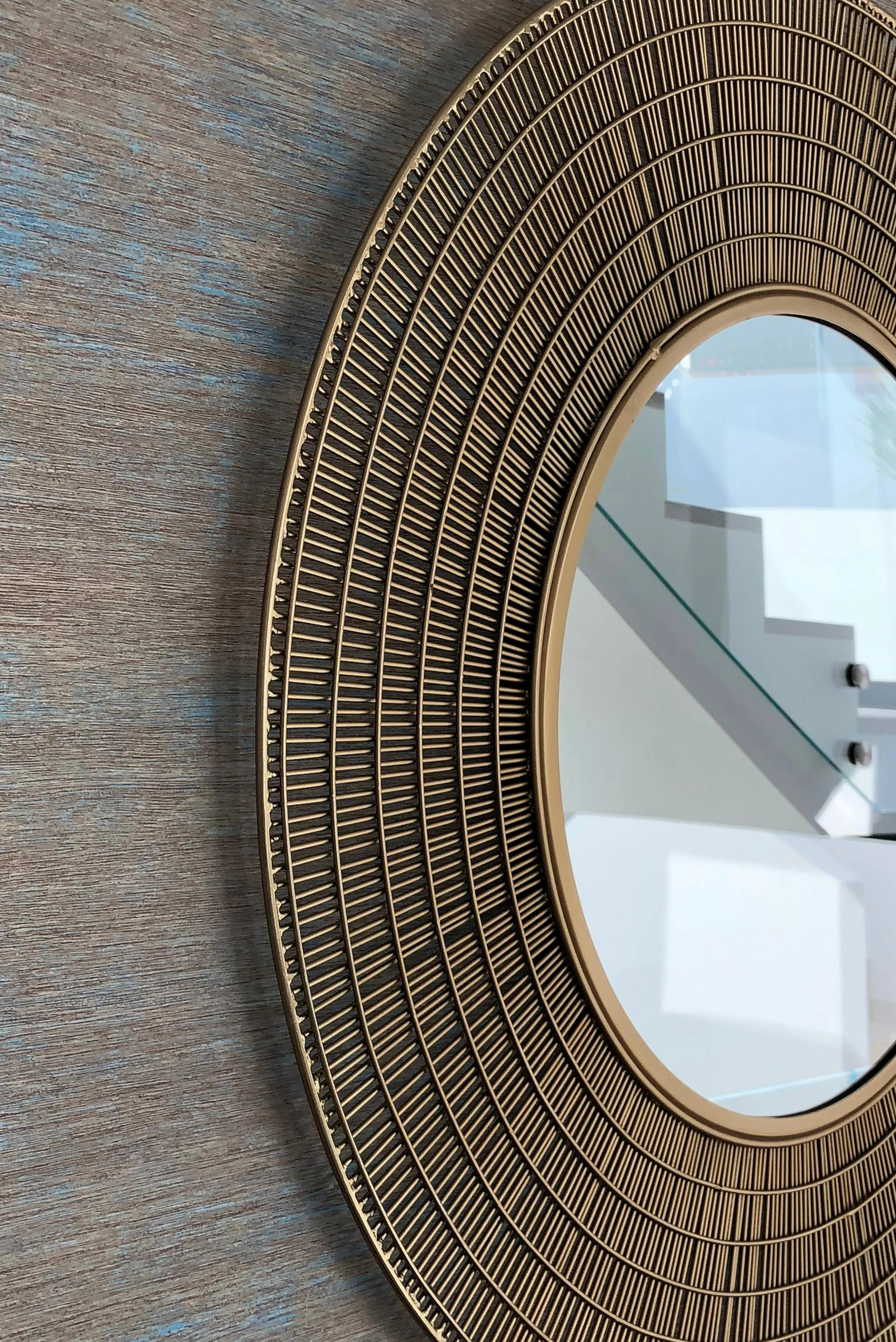 Close-up of a gold-colored circular decorative mirror or frame with an intricate, layered, and ribbed design, mounted on a wooden surface.