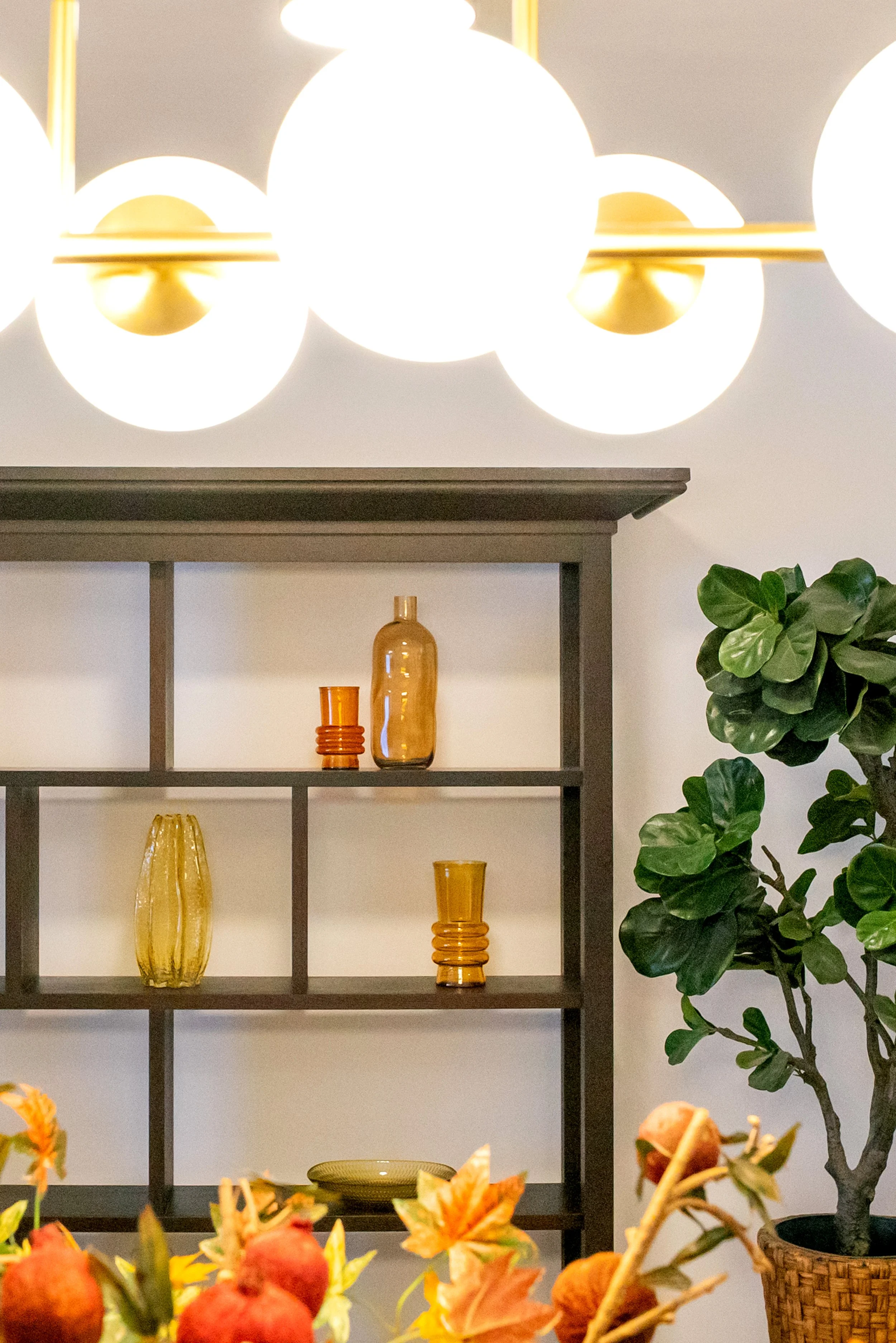 A modern interior with a black shelf displaying decorative vases in yellow and orange, and a large green houseplant on the right side.