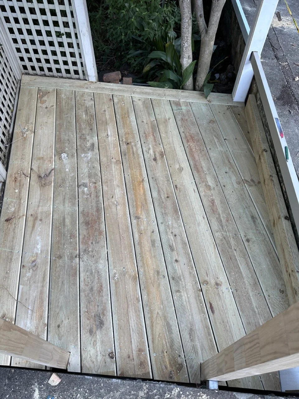 Newly constructed wooden deck with a lattice fence and some green plants in the background.