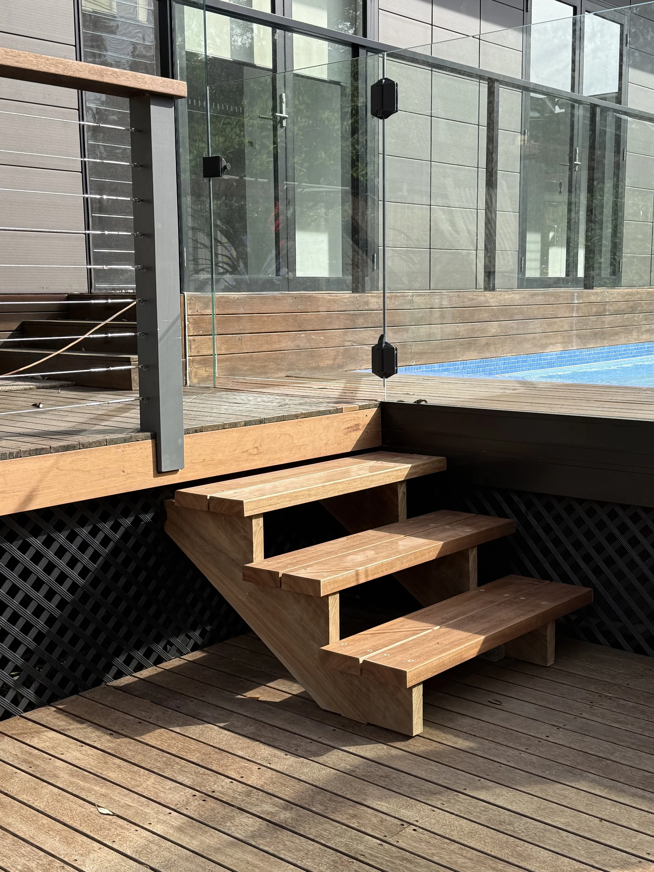 Wooden stairs on a deck leading up to a glass railing and a modern building with large windows.
