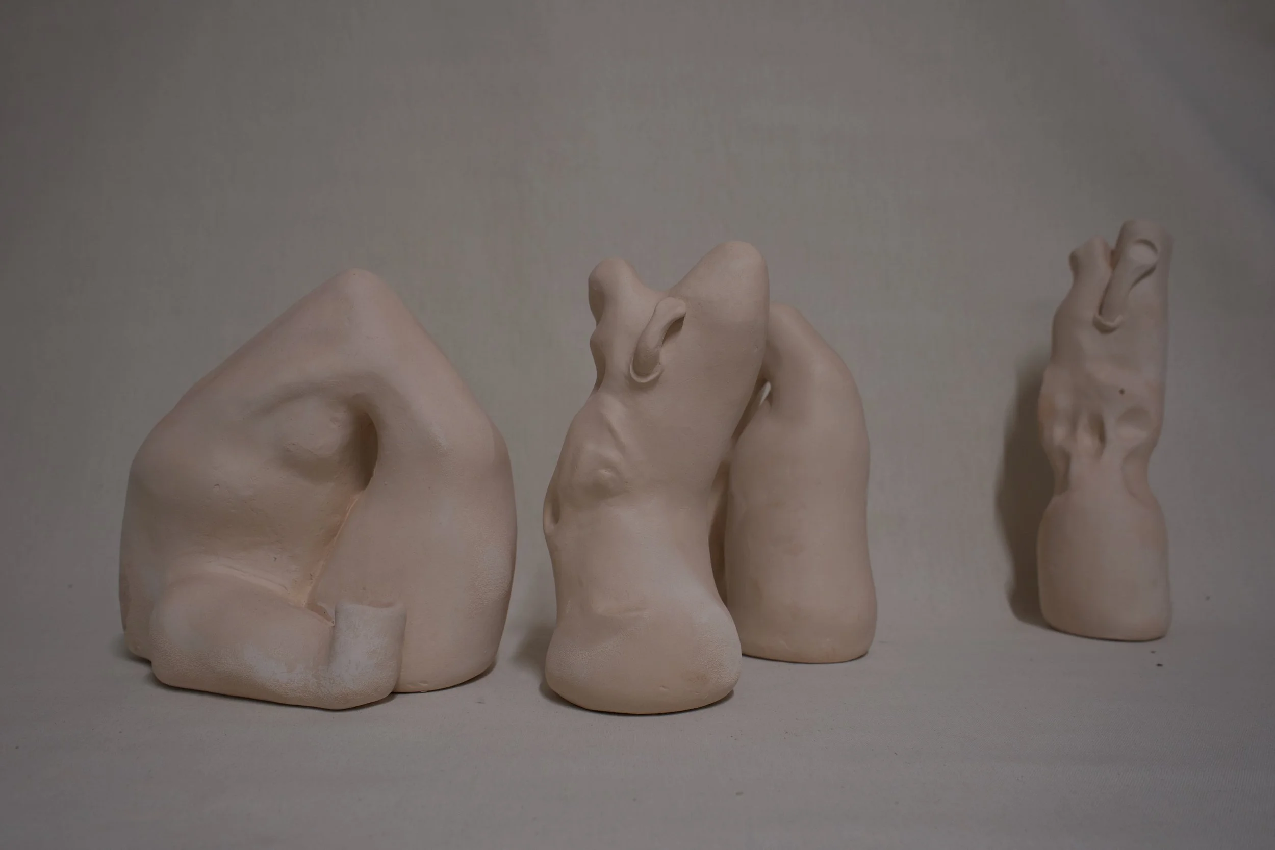 Drei abstrakte, skulpturartige Formen aus hellbeigem Material auf einer neutralen Oberfläche