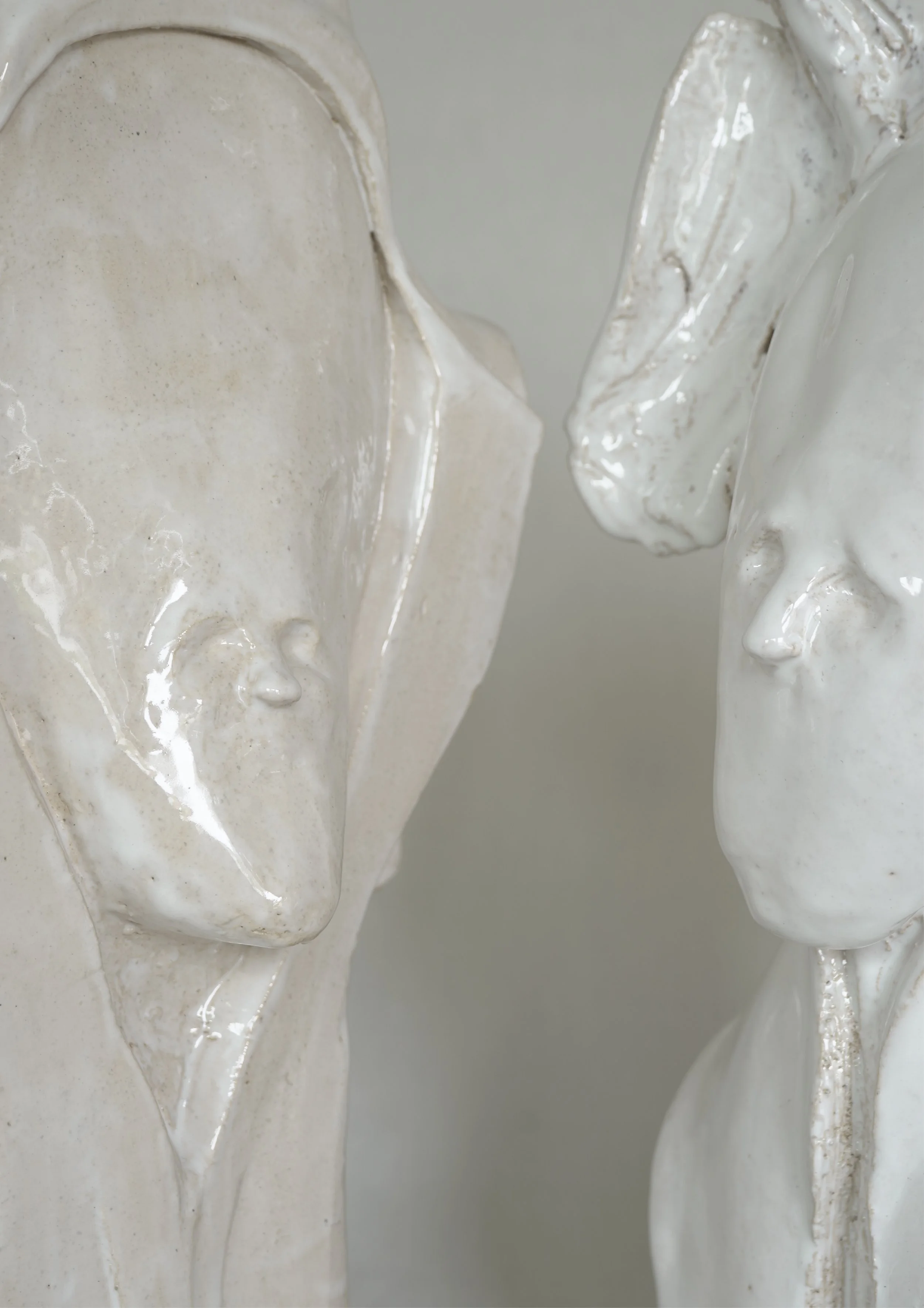 Zwei weiße Keramikstatuen, die Gesichter in Nahaufnahme zeigen, mit einem Fokus auf die Nasen und Lippen.