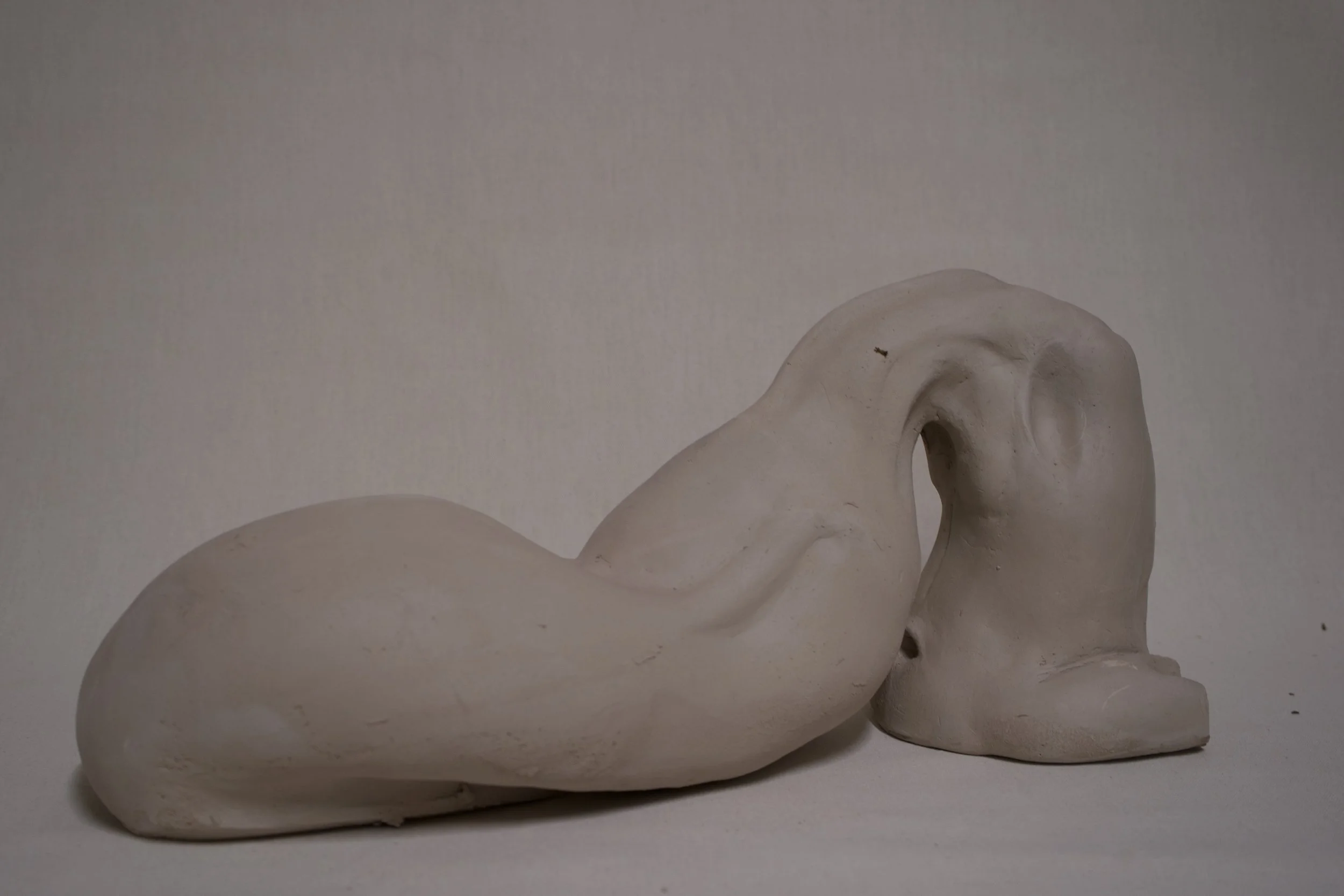 Kunststoffskulptur, die eine abstrakte Mischung aus menschlichem Gesicht und Tierkopf darstellt, vor neutralem Hintergrund.