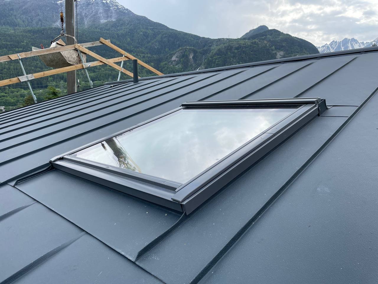 Finestra da soffitto su tetto in metallo con montagne e cielo nuvoloso sullo sfondo.