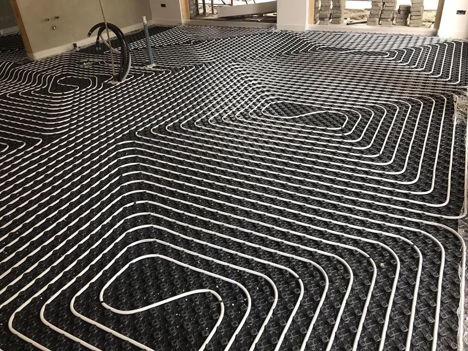 Sistemi di riscaldamento a pavimento in fase di installazione, con tubi bianchi disposti su una superficie nera.