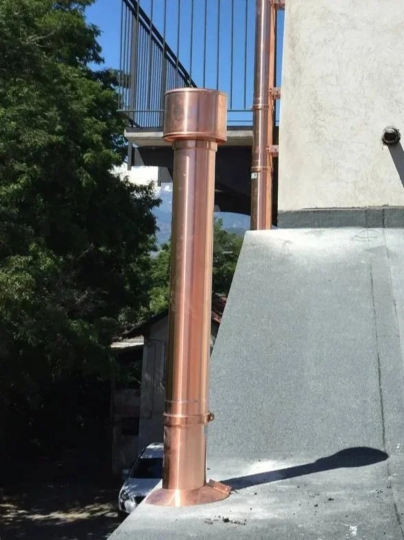 Scarico in rame di un edificio con un tubo verticale e un cappuccio, in un'area esterna soleggiata