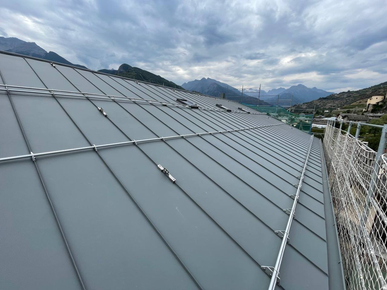 Vista del tetto di un edificio con pannelli solari, con montagne sullo sfondo e cielo nuvoloso.