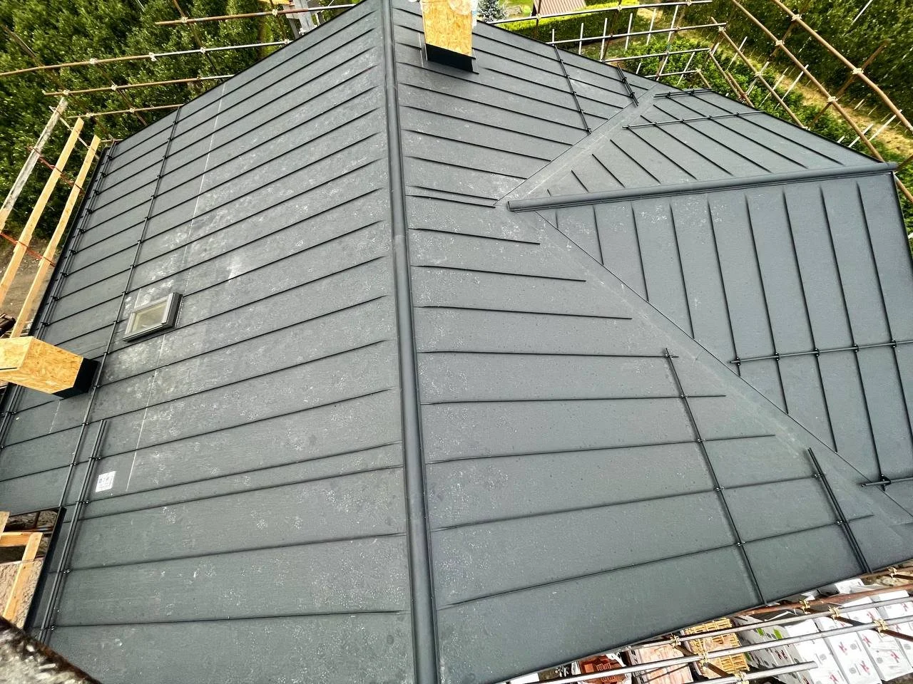 Tetto di una casa in costruzione con pannelli di copertura neri, torri di supporto in legno e una finestra sul lato.