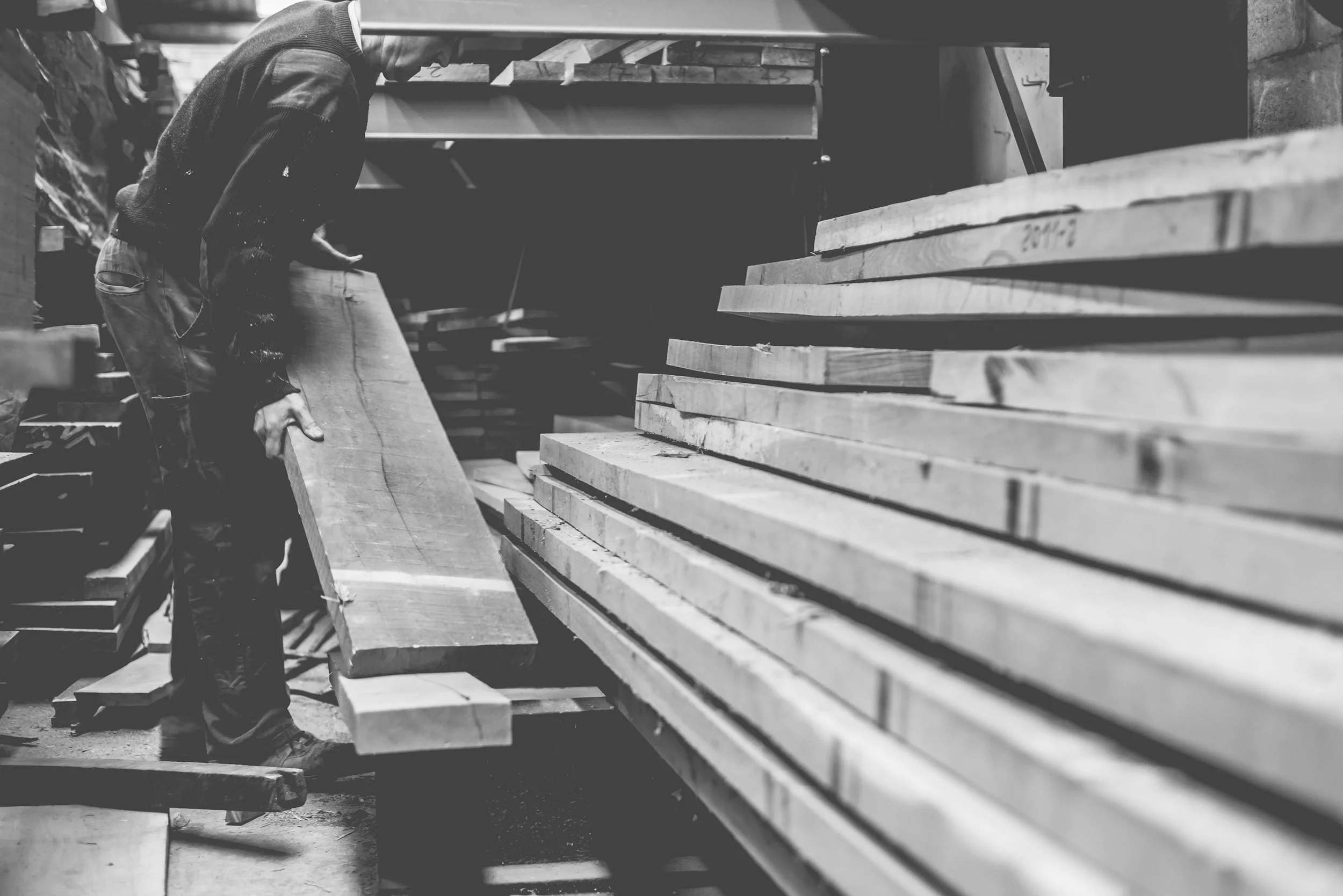 Persona en taller de carpintería con piezas de madera, trabajando con una tabla de madera.