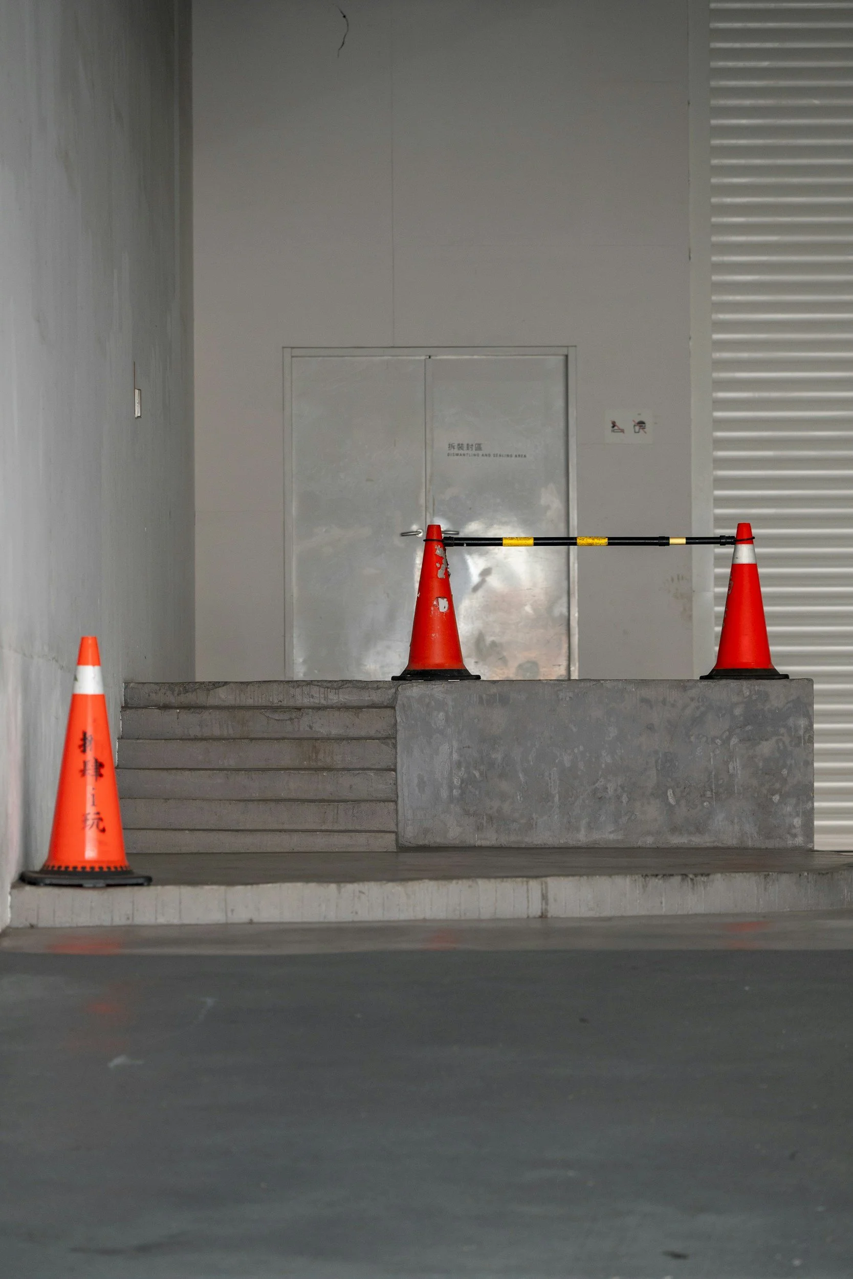 Concrete stairs with three orange traffic cones blocking access to a doorway in an industrial or parking garage setting.