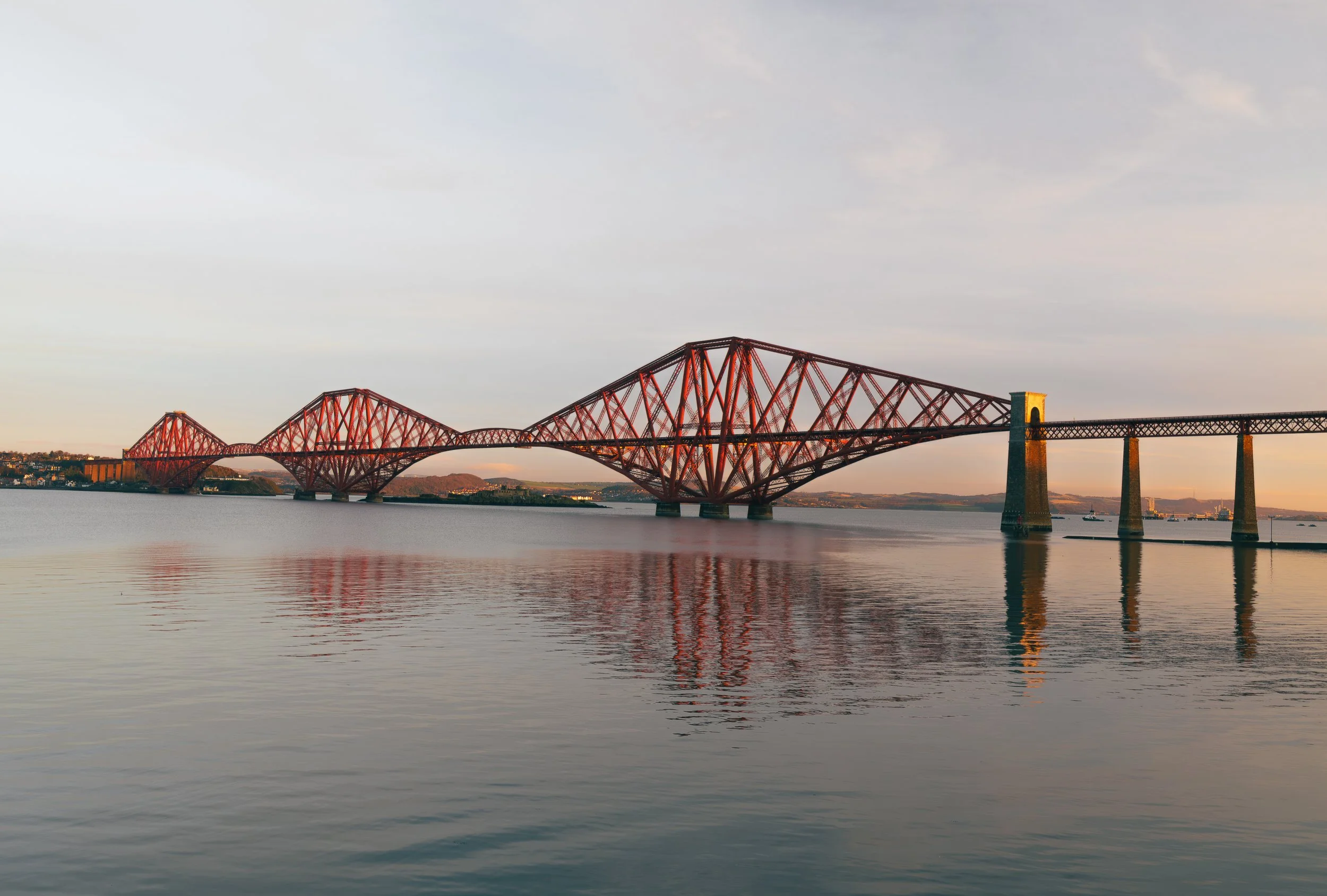 The Forth Bridge at sunrise, stretching over the calm waters of the Firth of Forth.