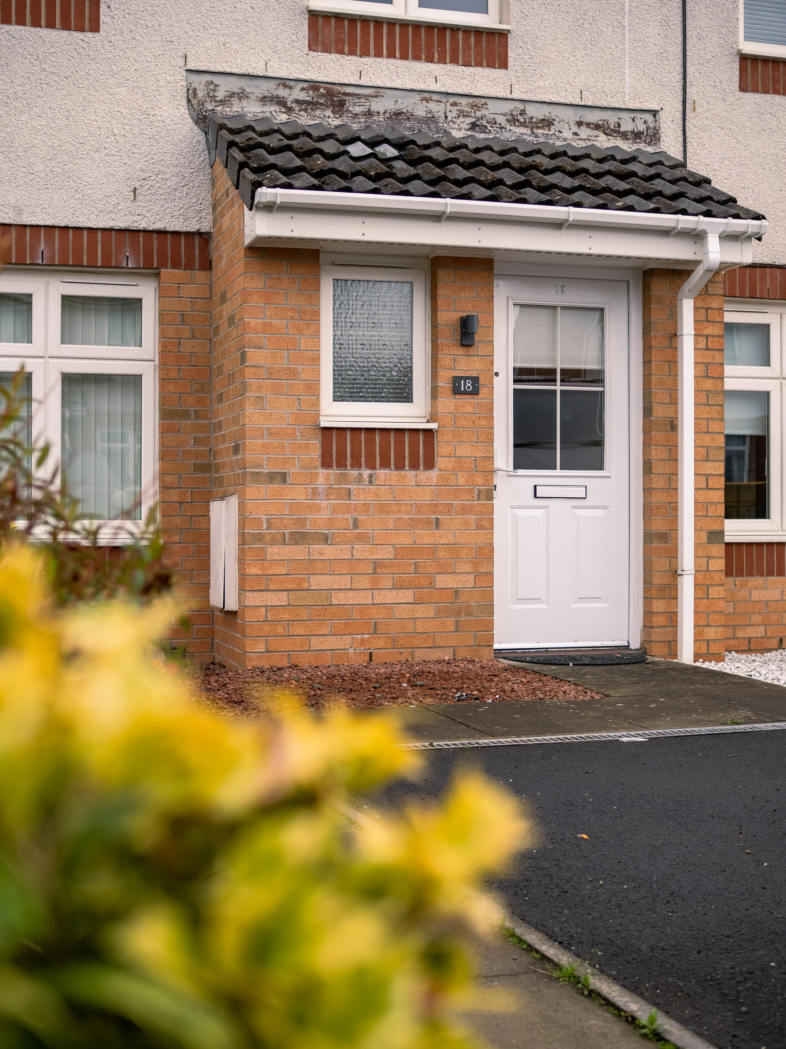 Front view of a brick residential house with a white front door, small window, and gabled roof.