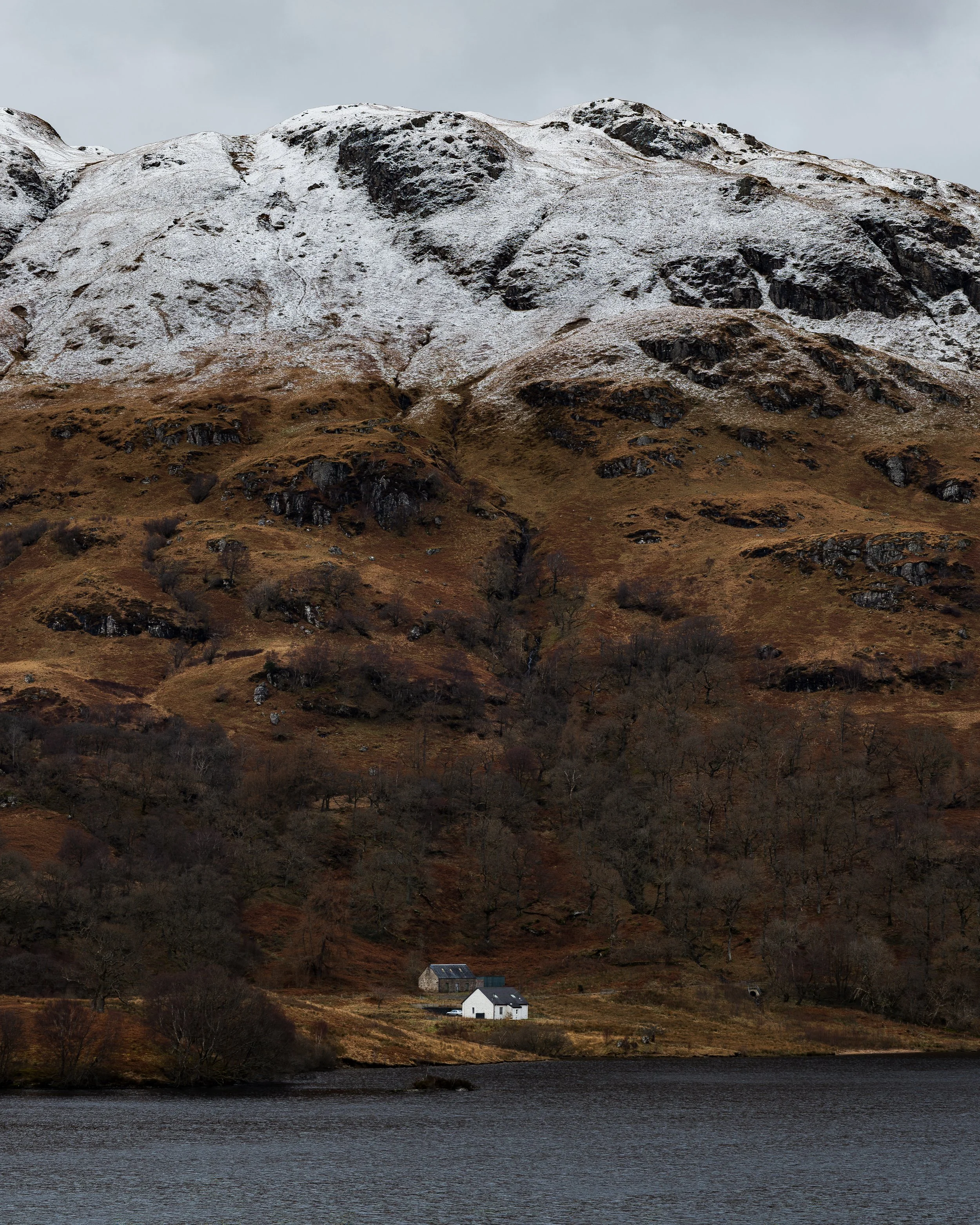 A small white cottage and farm building on the shores of Loch Katrine.