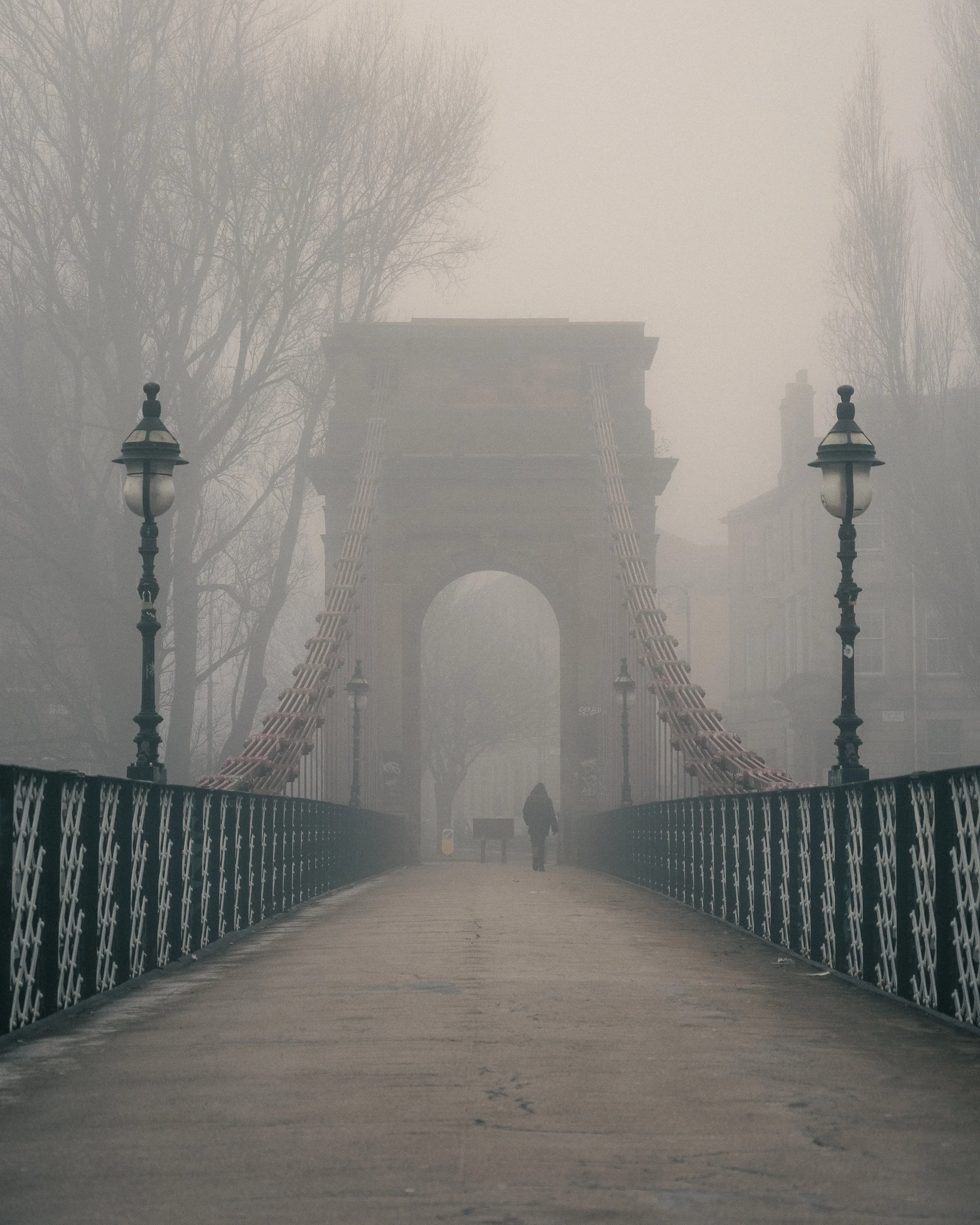 A foggy scene of the Chain Bridge with a person walking in the distance.