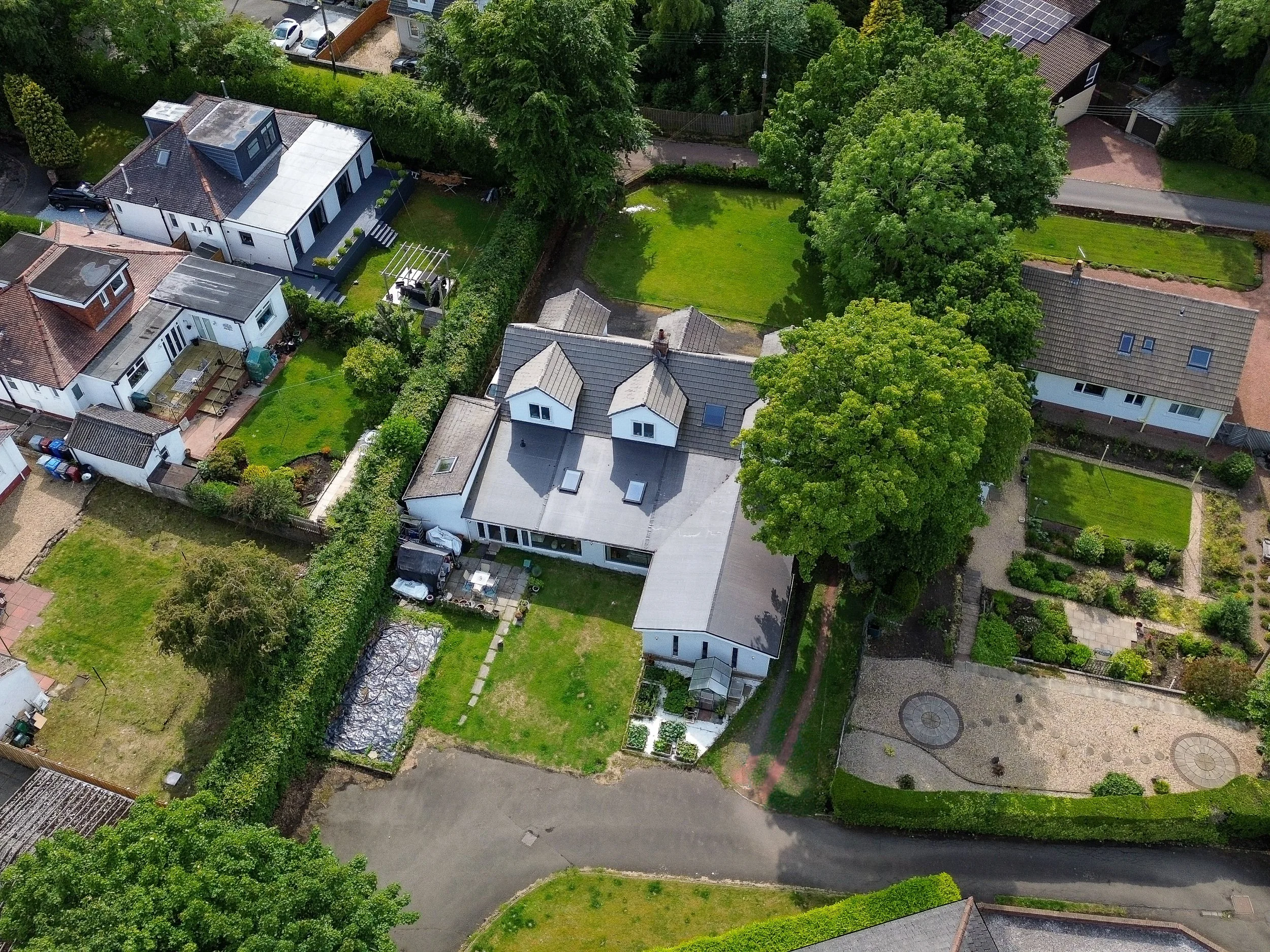 An aerial view of a residential neighborhood showing multiple houses with gardens, trees, and a curved road.