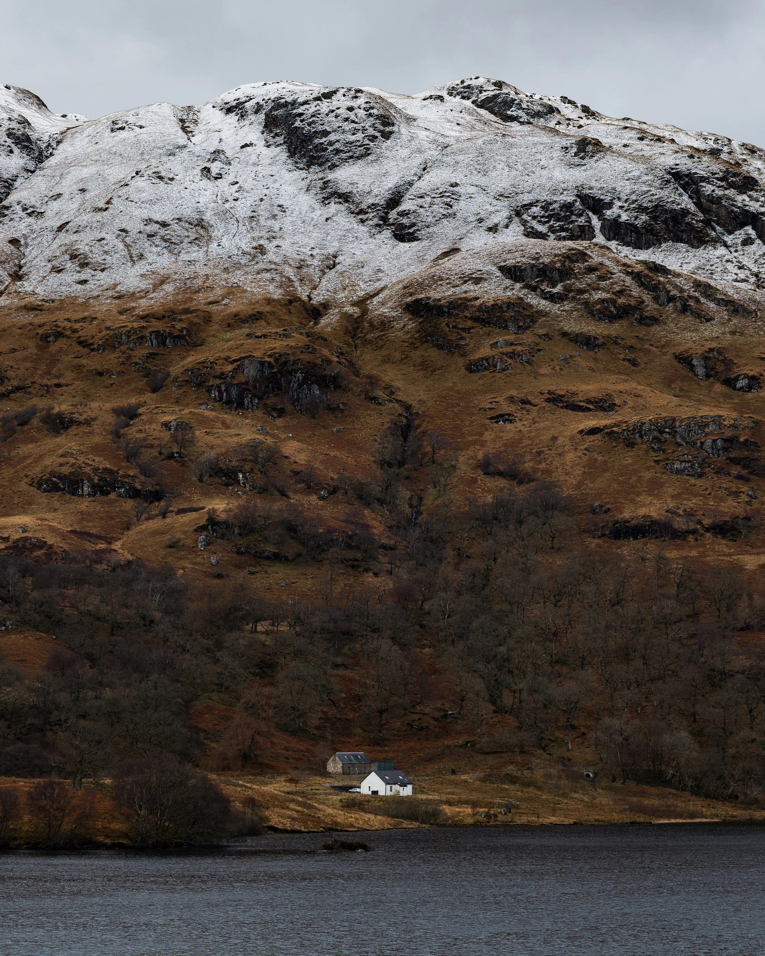 A small white cottage and farm building on the shores of Loch Katrine.