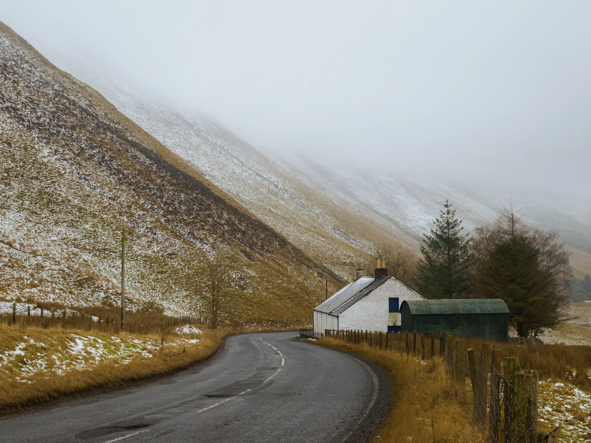 A white cottage and farm shed along the Dalveen Pass, with snow and mist covered hills.