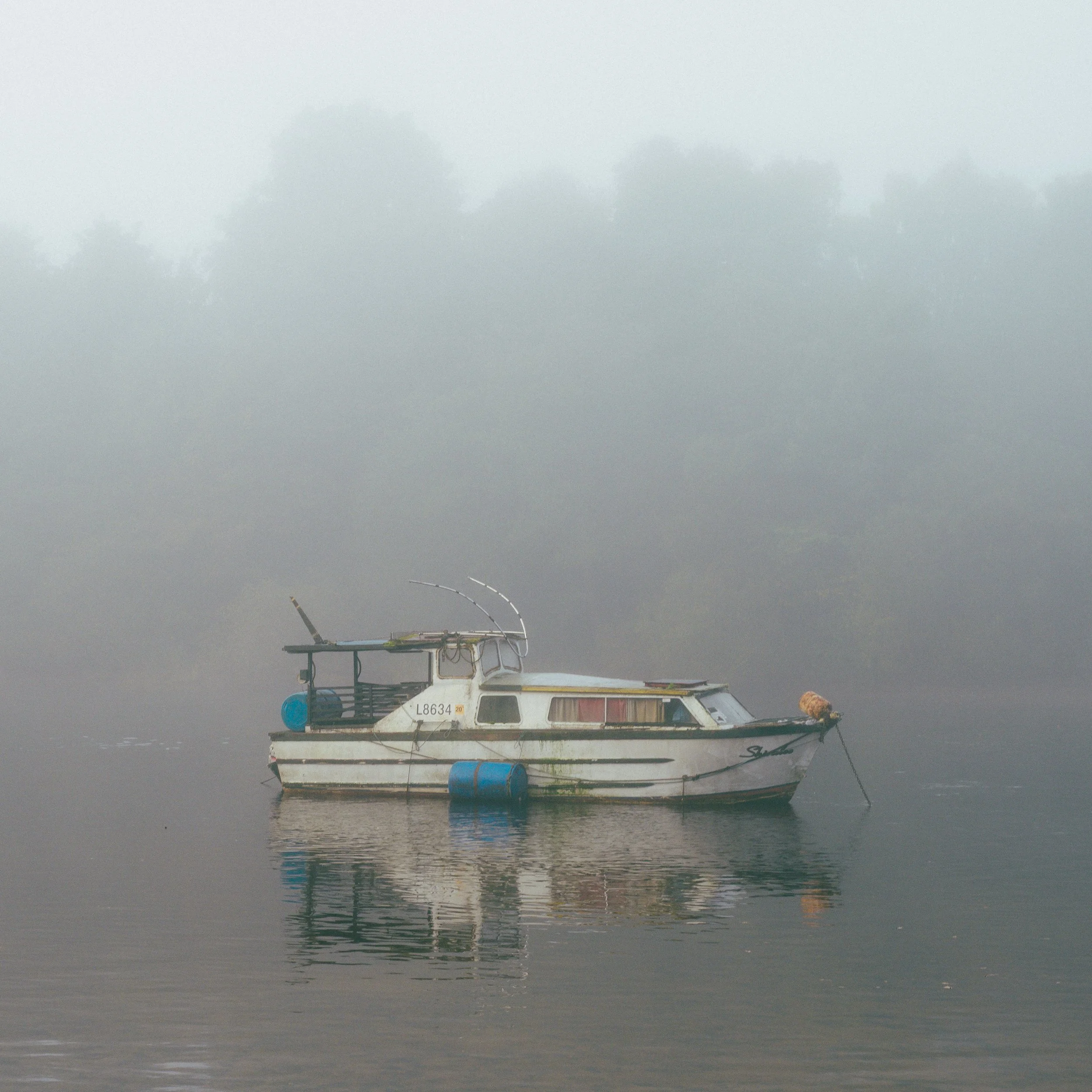 A boat floating on Loch Lomond with foggy trees in the background.