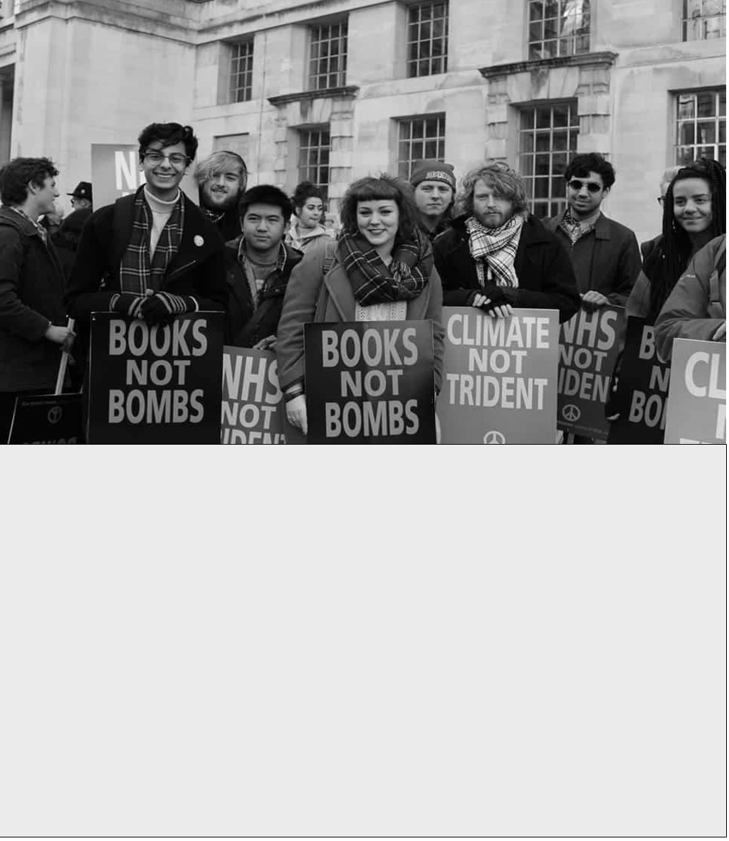 Group of people holding protest signs that read "Books Not Bombs" and "Climate Not Trident" during a demonstration outside a government building.