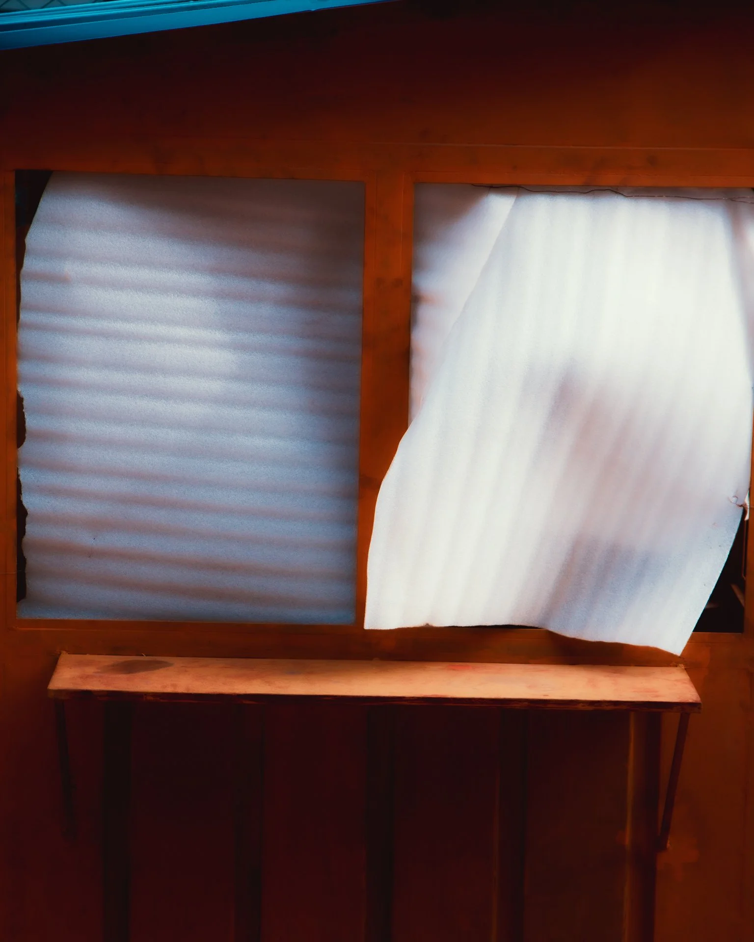 A wooden window frame with two different types of window coverings: one window with horizontal blinds and the other with a curtain partially pulled aside.