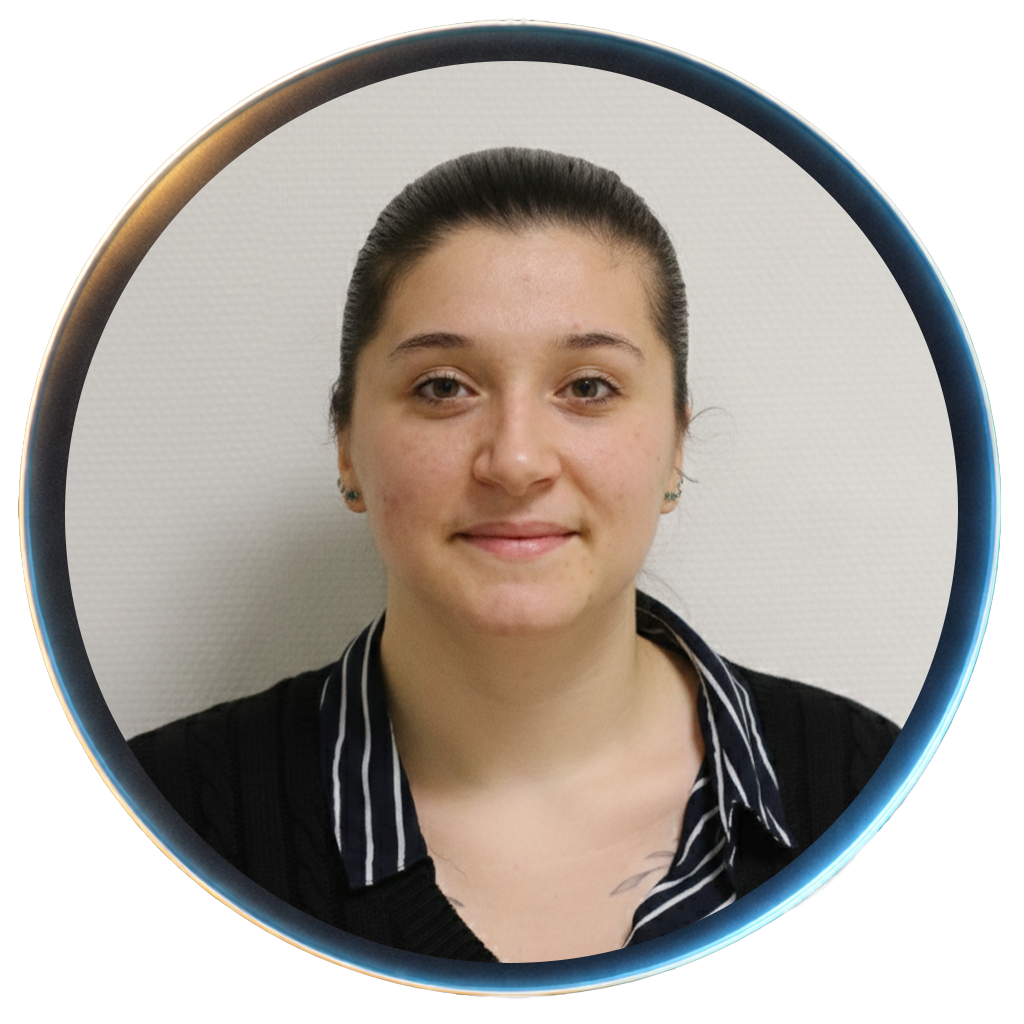 A woman with short dark hair smiling in a laboratory setting, wearing a black sweater and gold jewelry.