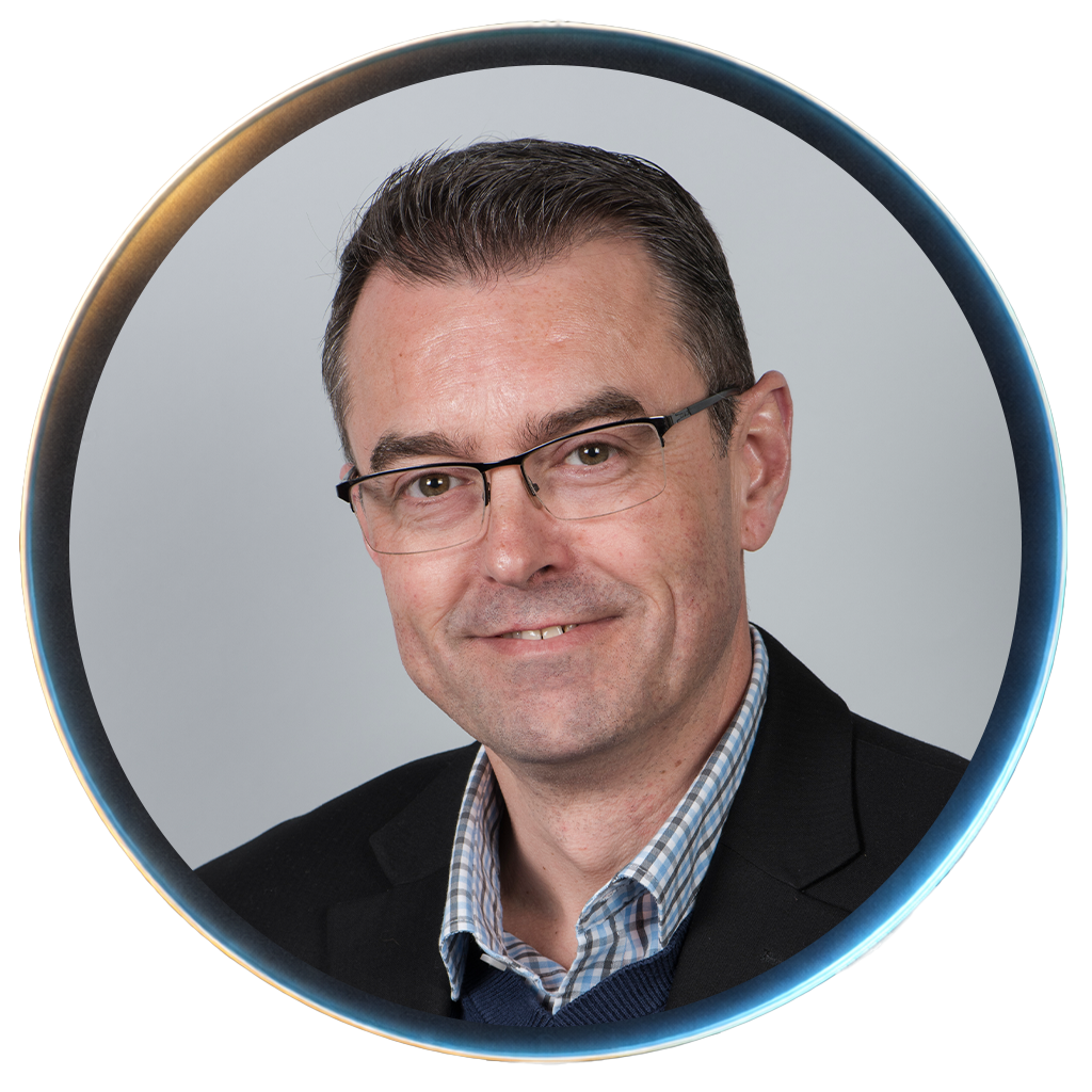 Professional portrait of a man with glasses, wearing a suit and checked shirt, smiling against a light gray background.