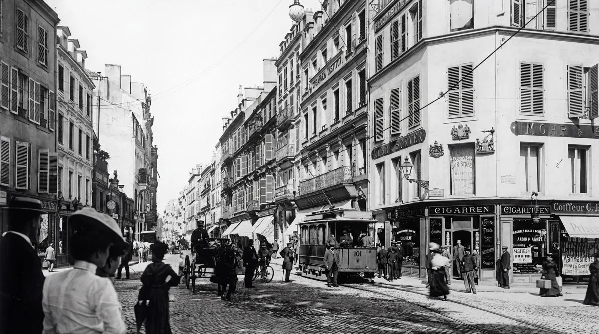 Une rue animée à Paris avec tramway, voitures, personnes marchant et commerces en arrière-plan.