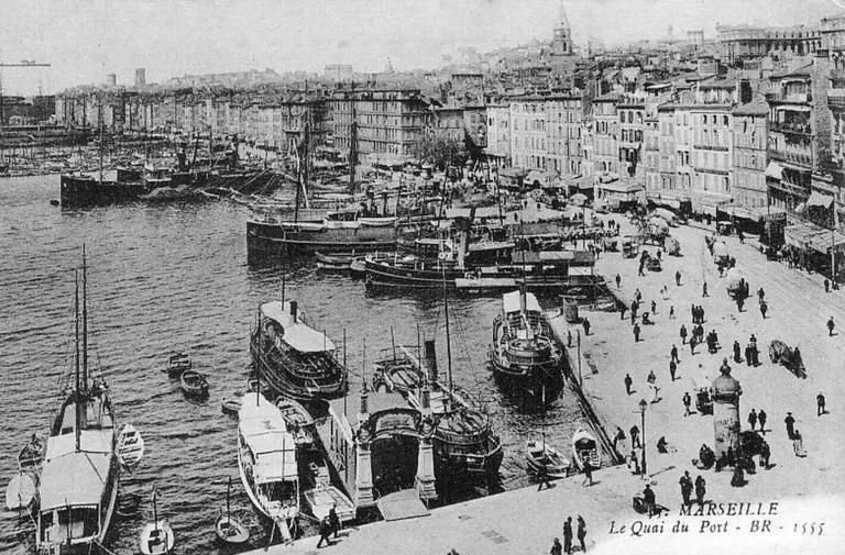 Une vue en noir et blanc du quai du port à Marseille en 1855, avec plusieurs bateaux amarrés et des gens se promenant sur le quai.
