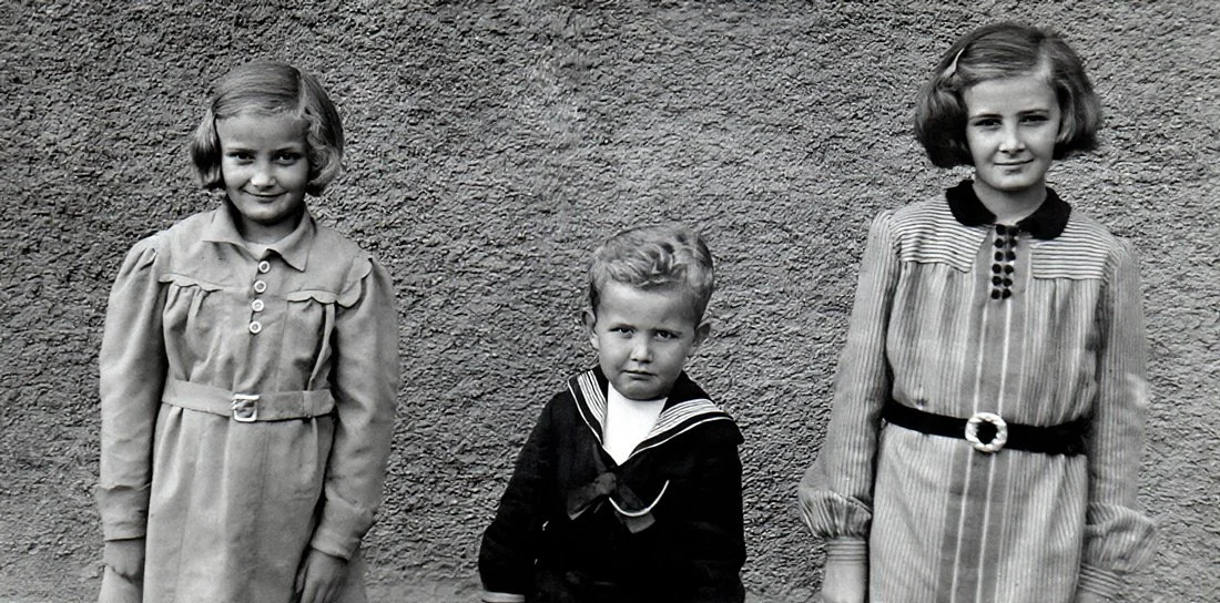 Trois enfants en vêtements d'époque posant devant un mur texturé.