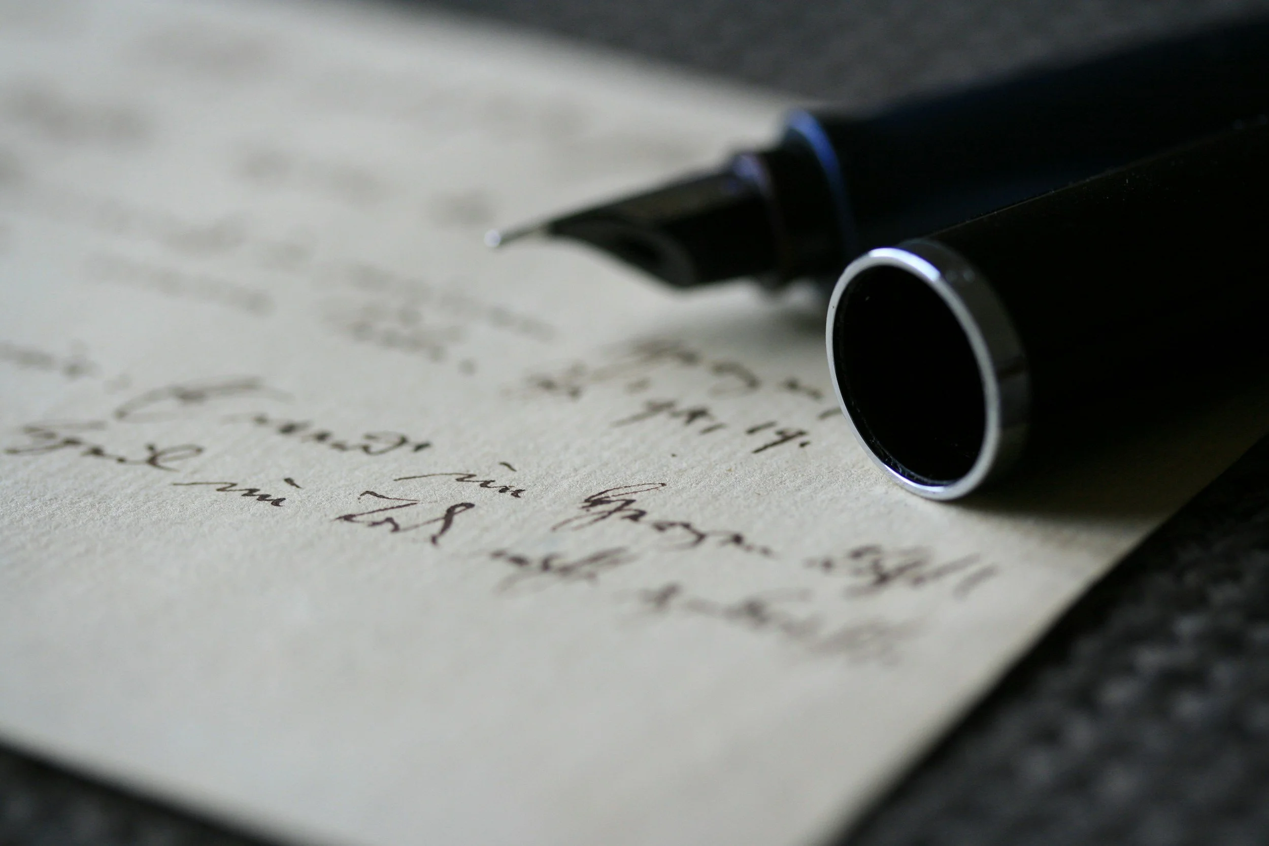 Close-up of a black fountain pen resting on handwritten letter paper with cursive writing.