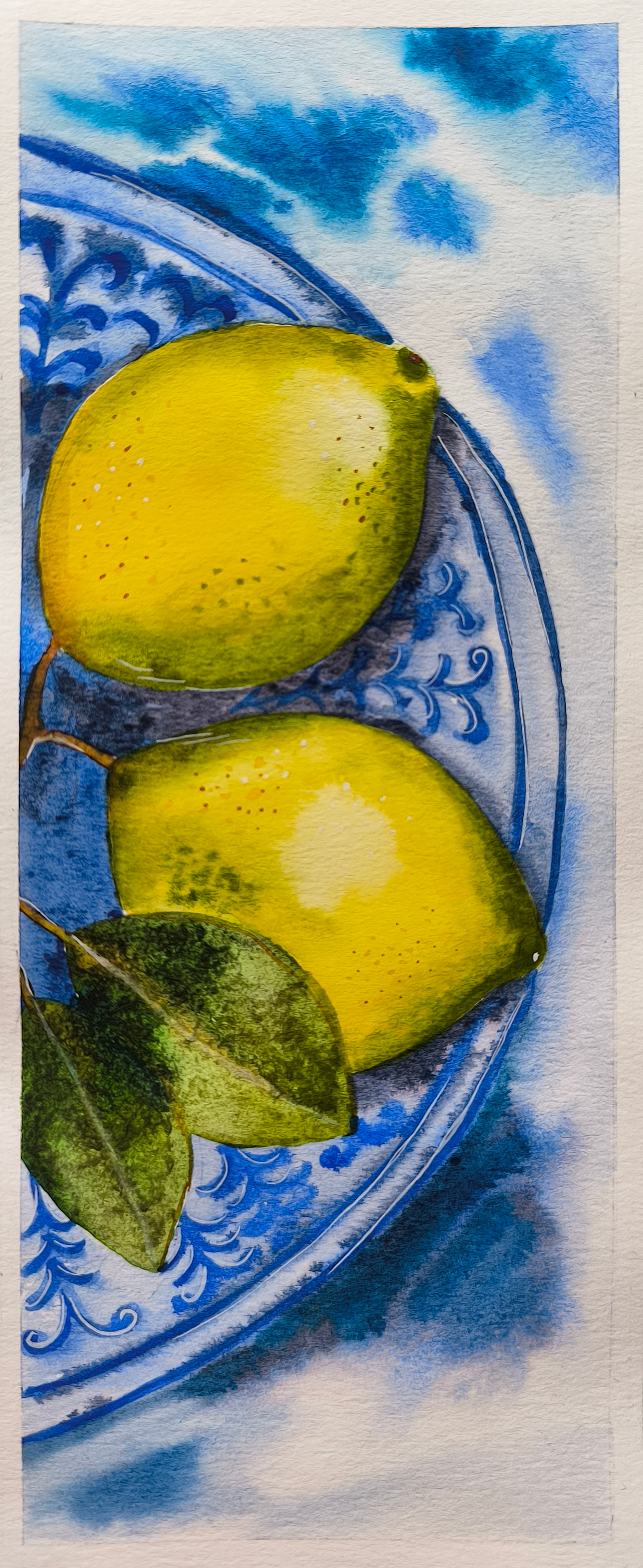 Watercolor painting of two yellow lemons and green leaves on a decorative blue and white plate.