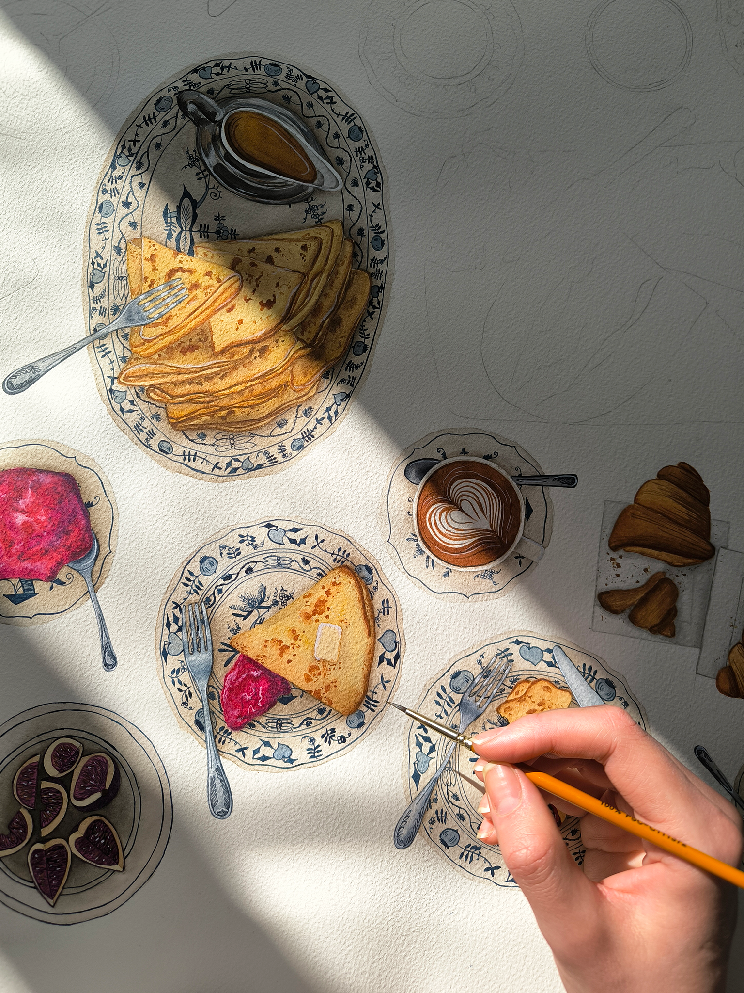 Photo of painted breakfast dishes on a white surface, including plates of pancakes, a slice of cake with pink topping, a small bowl of figs, a cup of coffee with latte art, and a hand holding a paintbrush adding details to the painting.