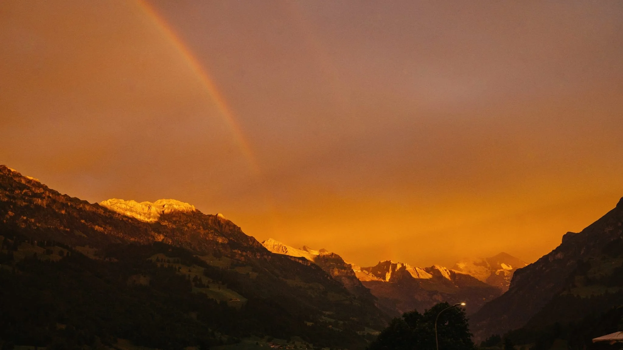Berglandschaft bei Sonnenuntergang mit Regenbogen am Himmel.