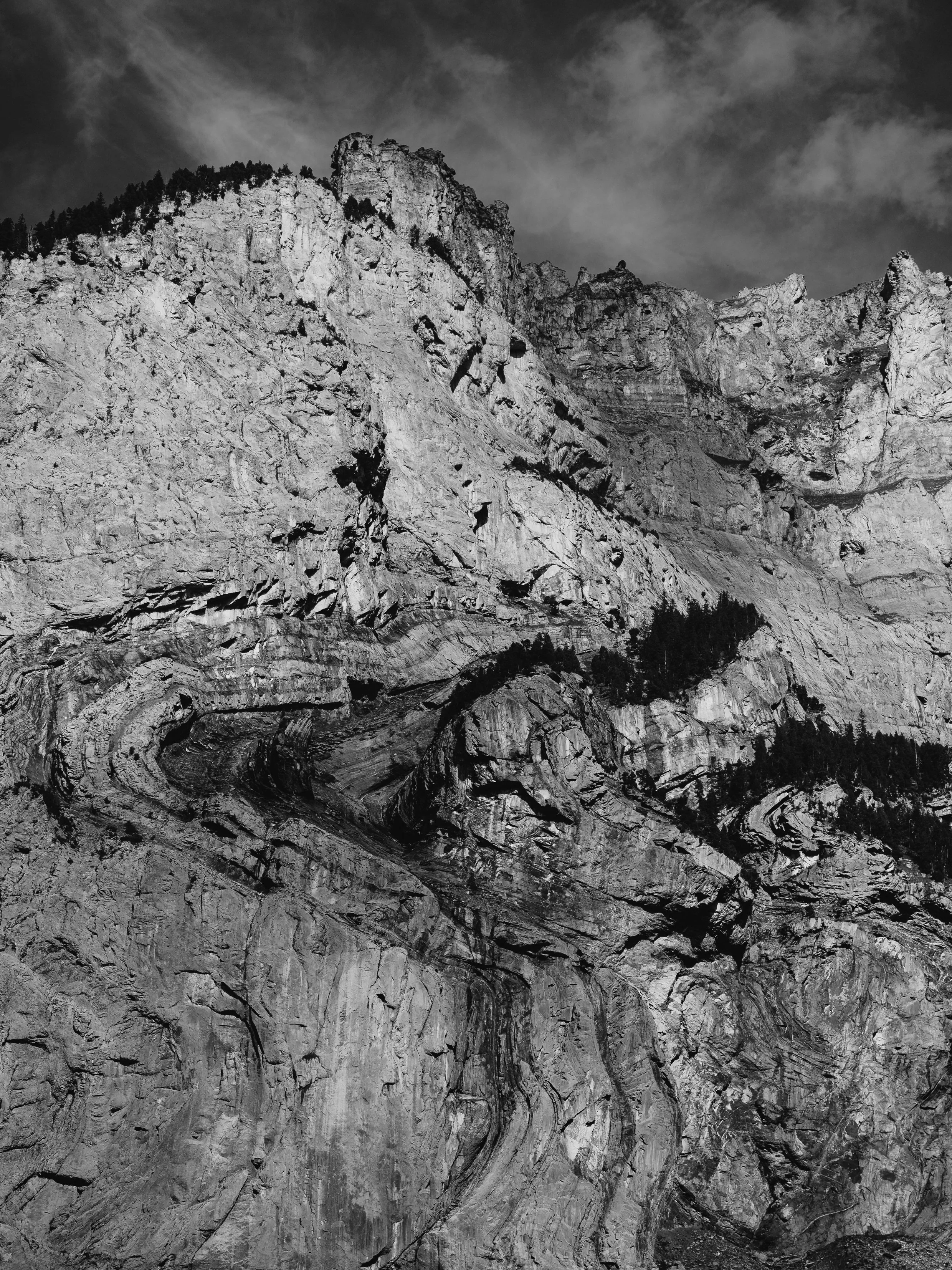 Schwarze und weiße Aufnahme eines Felsgewölbes mit schroffen Felsen und Kiefern auf dem Felsen