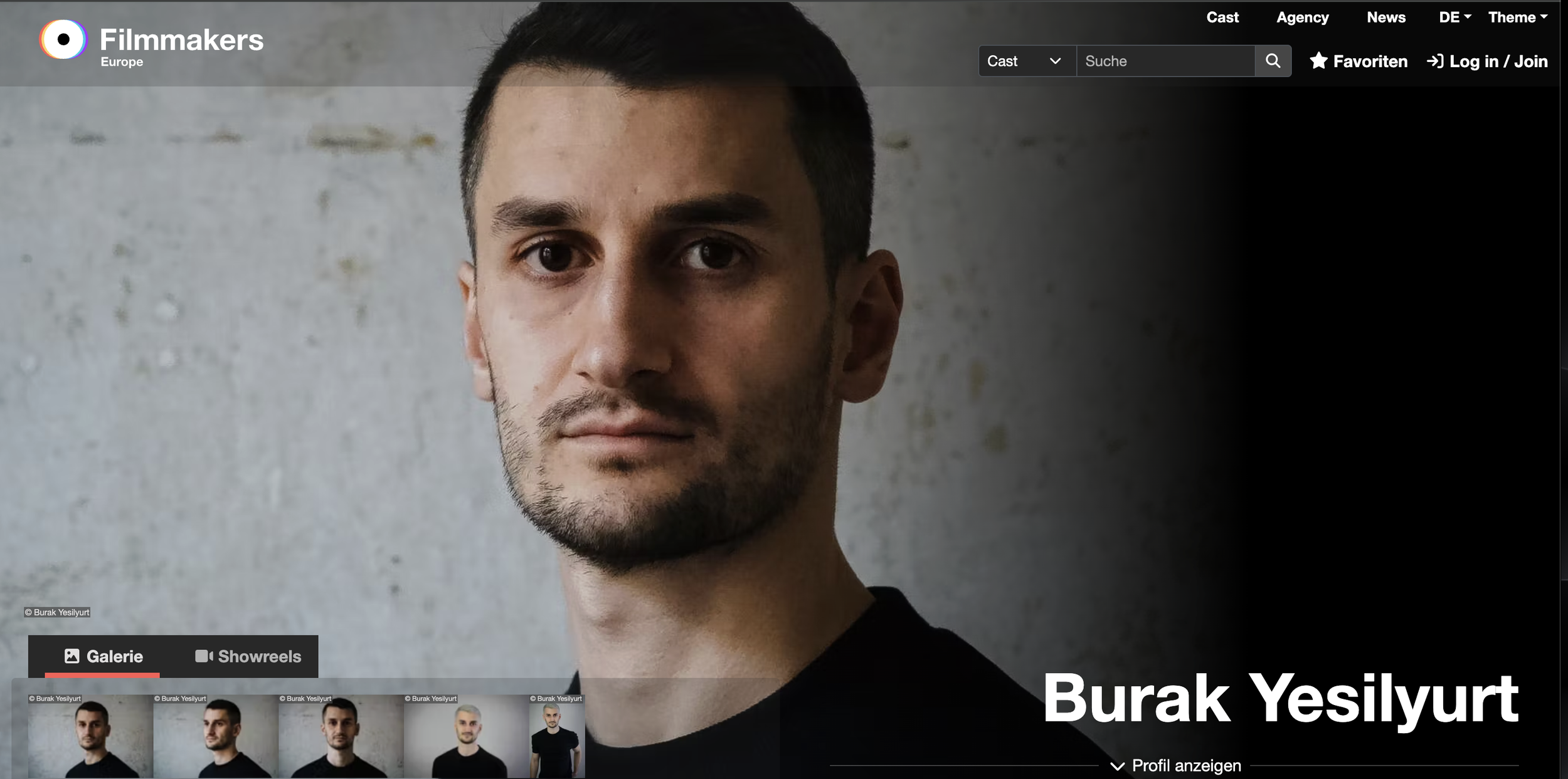 Porträt eines jungen Mannes mit dunklem Haar und Bart, trägt ein schwarzes T-Shirt, steht vor einer grauen Wand.