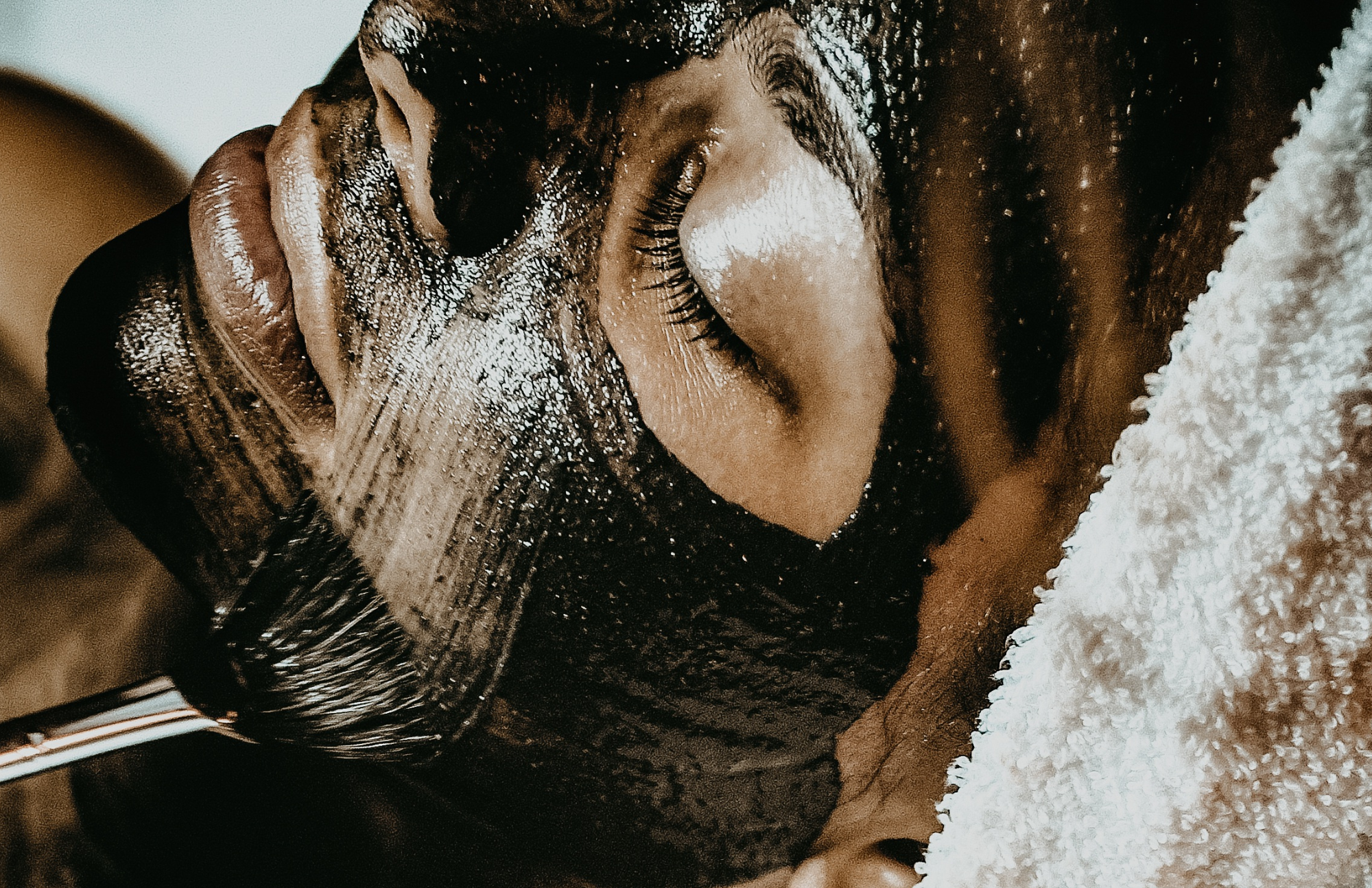 Person with their eyes closed having their face washed or massaged, covered in soap lather, with a white towel nearby.