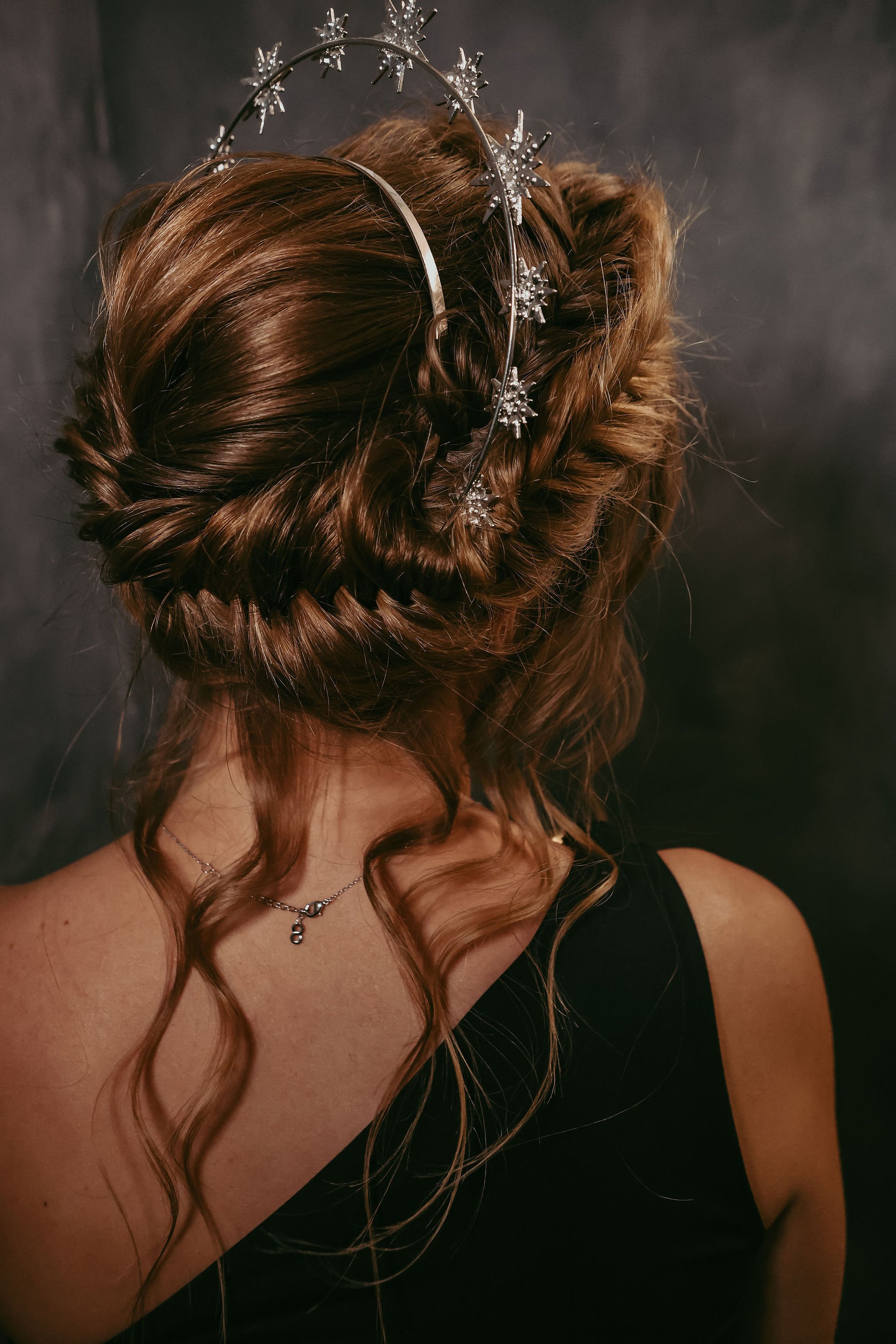 A woman with brown hair styled in an elegant updo, wearing a silver star-themed headband, with loose curls and a black dress.