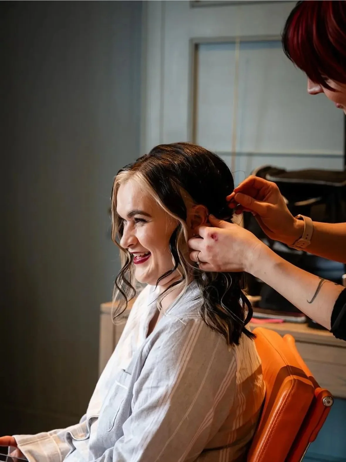 Woman smiling while getting her hair styled by a hairstylist.