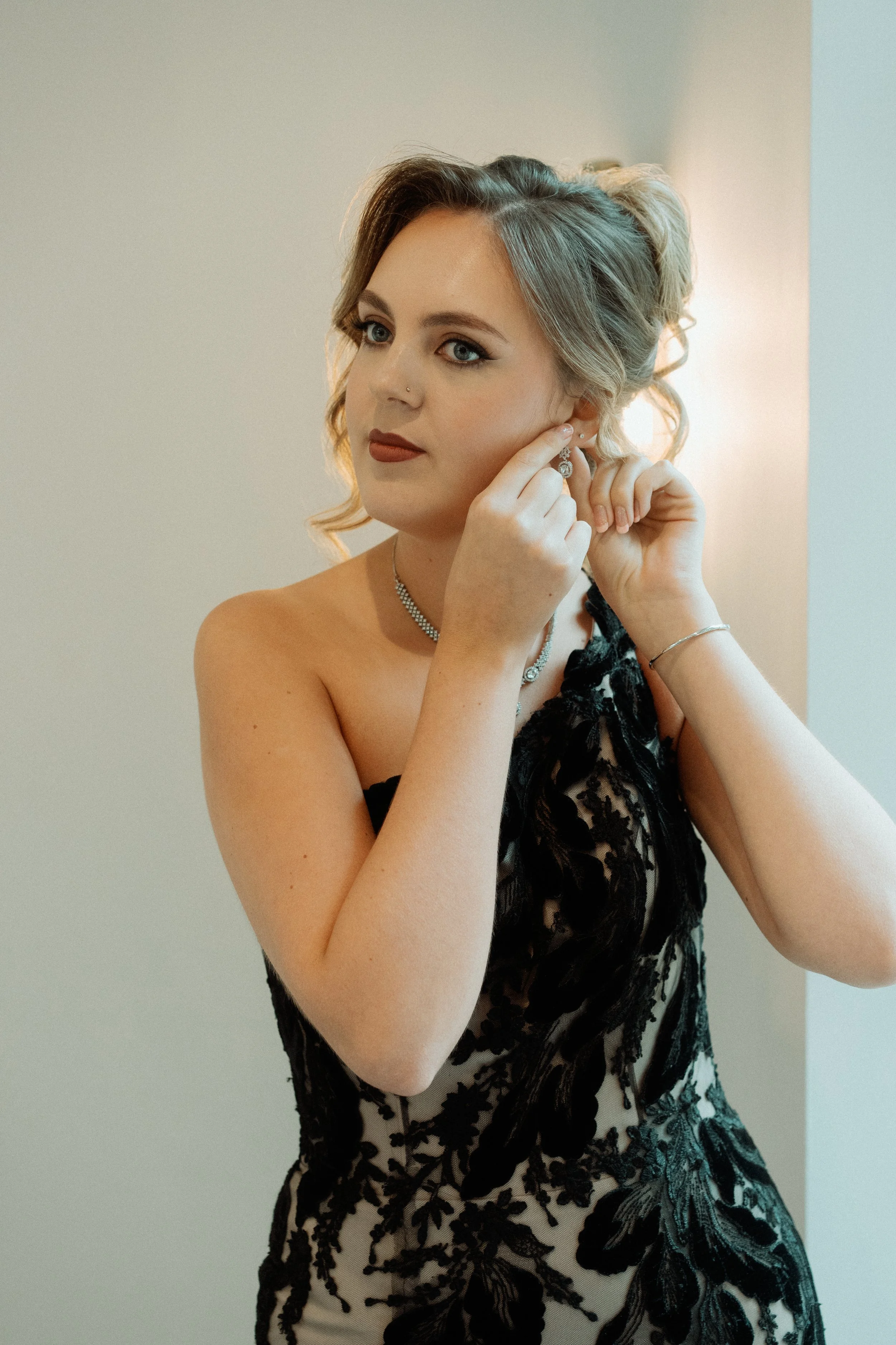 A woman in a black lace dress adjusting her earring.