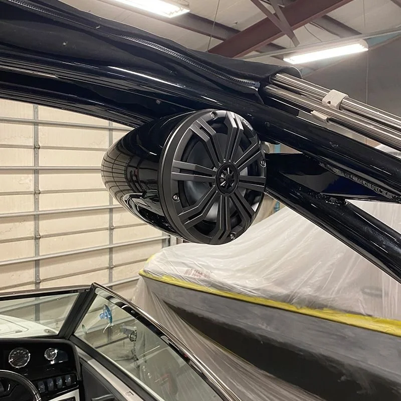 Close-up of a large black boat speaker mounted under the boat's canopy, with a car and a garage door in the background.