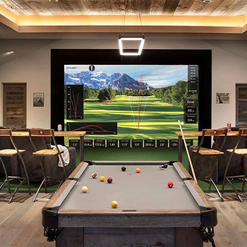 Indoor golf simulation room with a large screen displaying a golf course, a pool table with billiard balls, and chairs along the sides.