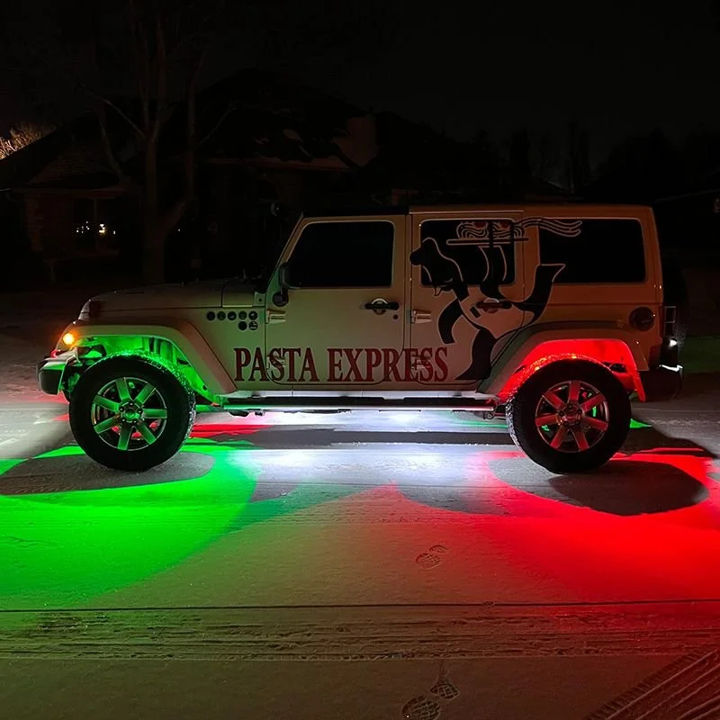 A beige SUV with 'Pasta Express' logo and a pasta dog graphic parked on a snow-covered street at night, illuminated by green and red lights.