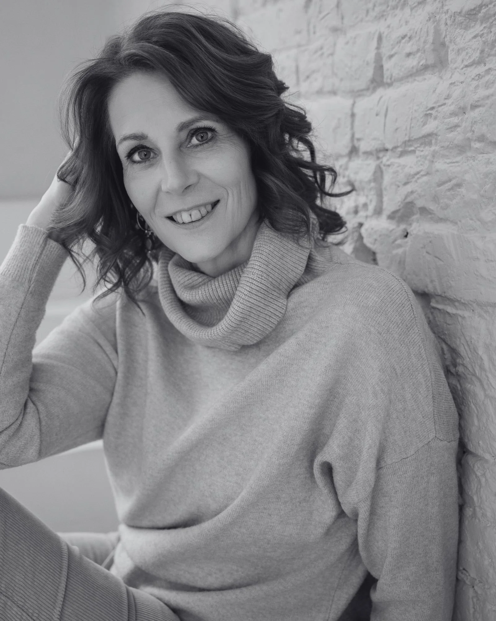 Zwart-witportret van Geke, 57, ontspannen tegen de witte bakstenen muur van het atelier in Lichtervelde