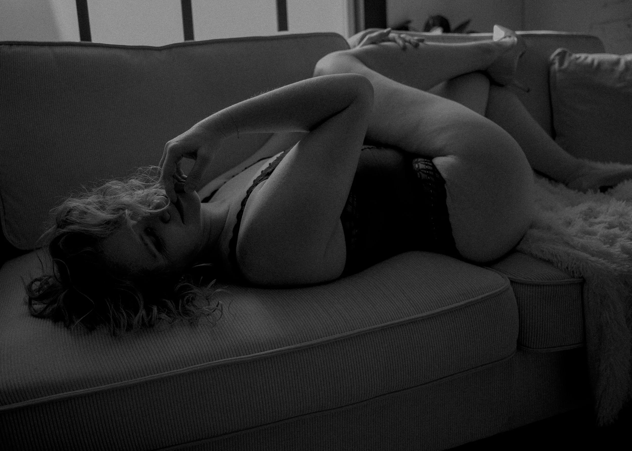 Een vrouw die op een sofa ligt met gesloten ogen, een kanten top en short draagt, deels bedekt met een deken.