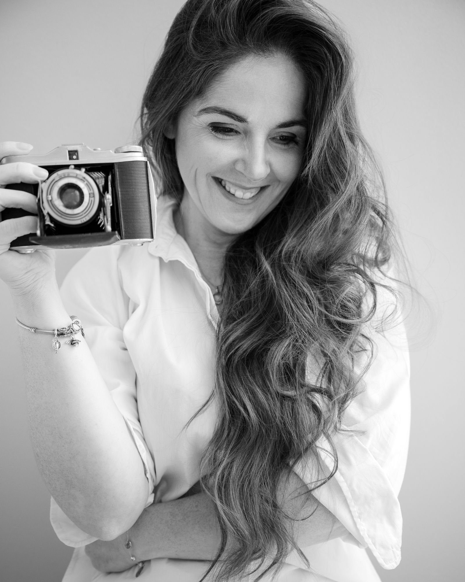 Zwart-witportret van Nathalie, 48, met een vintage fototoestel voor haar oog