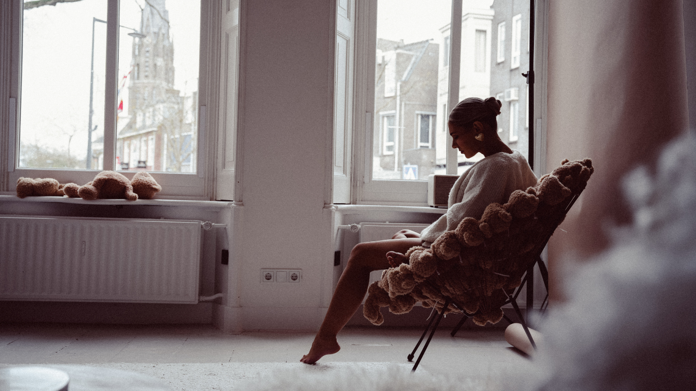 Woman relaxing barefoot in a teddy bear-covered chair beside a sunlit window