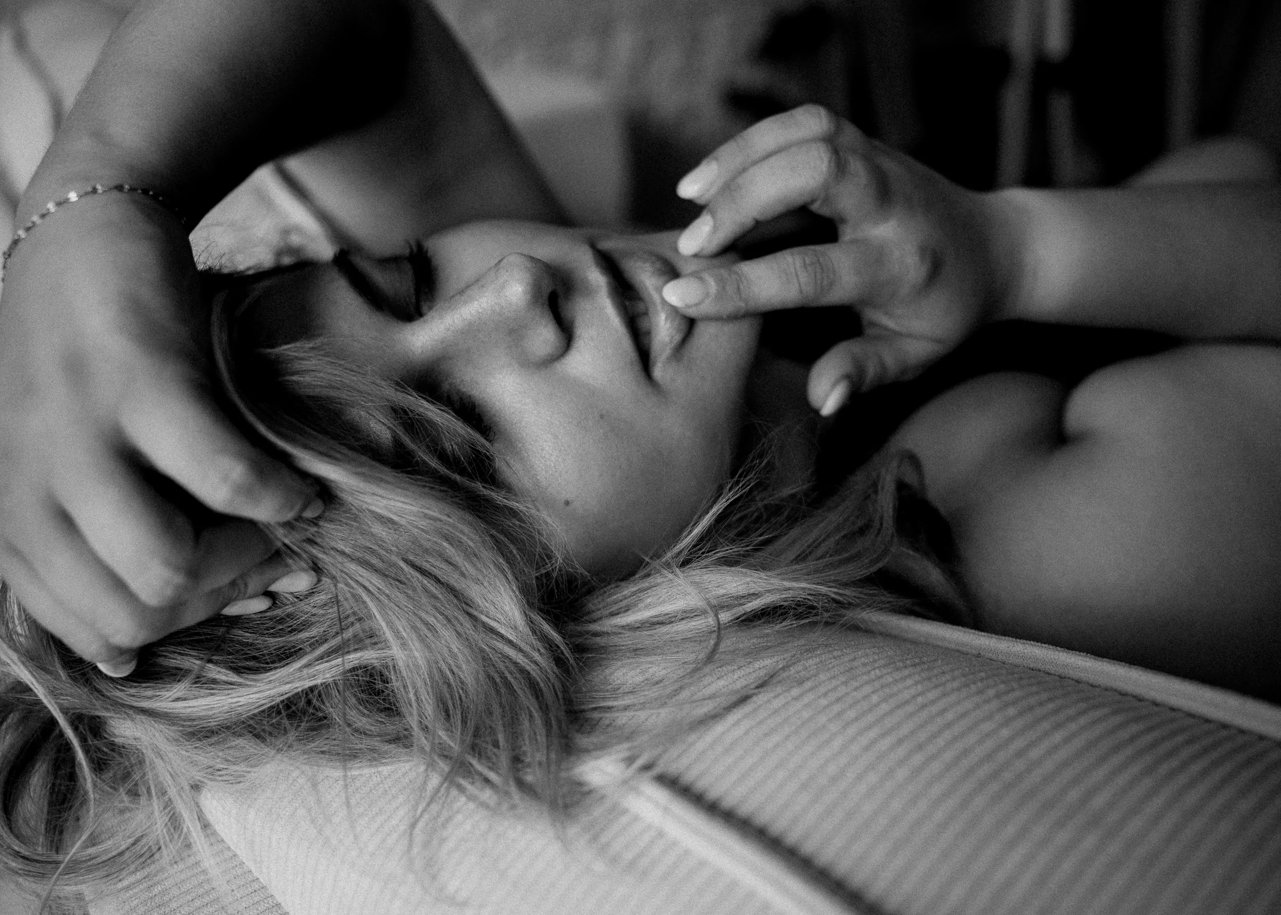 Zwart-wit foto van een vrouw die ligt met gesloten ogen, haar hoofd rustend op een oppervlak, terwijl ze zachtjes haar lippen aanraakt met haar vingers.