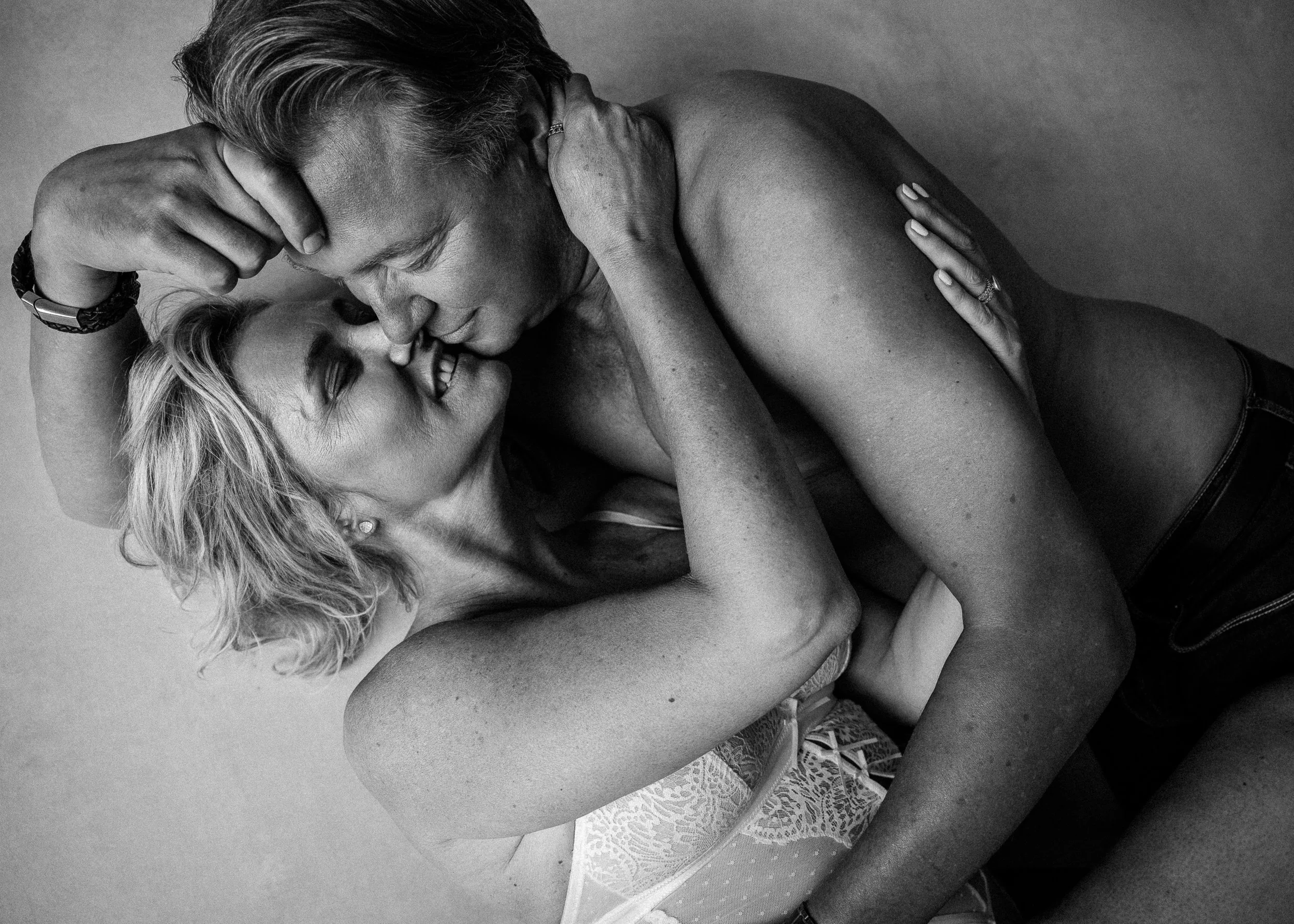 Zwart-wit foto van een koppel in een intieme omhelzing, hun gezichten dicht bij elkaar terwijl ze glimlachen en liefde en tederheid tonen.